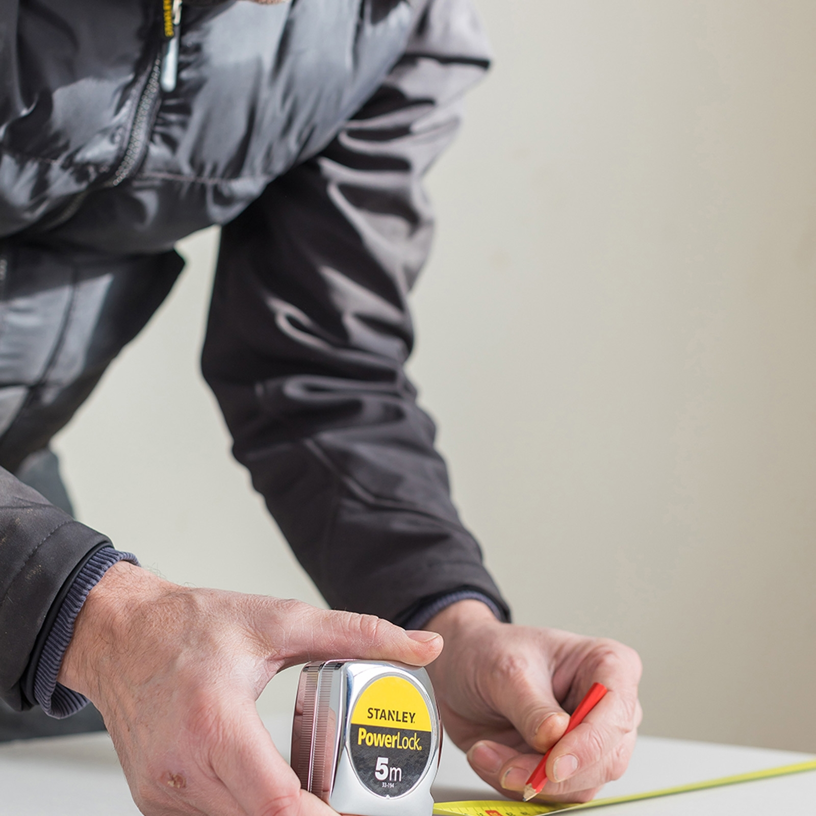 Osoba mierzy taśmą mierniczą Stanley Powerlock i czerwonym ołówkiem na białej powierzchni.