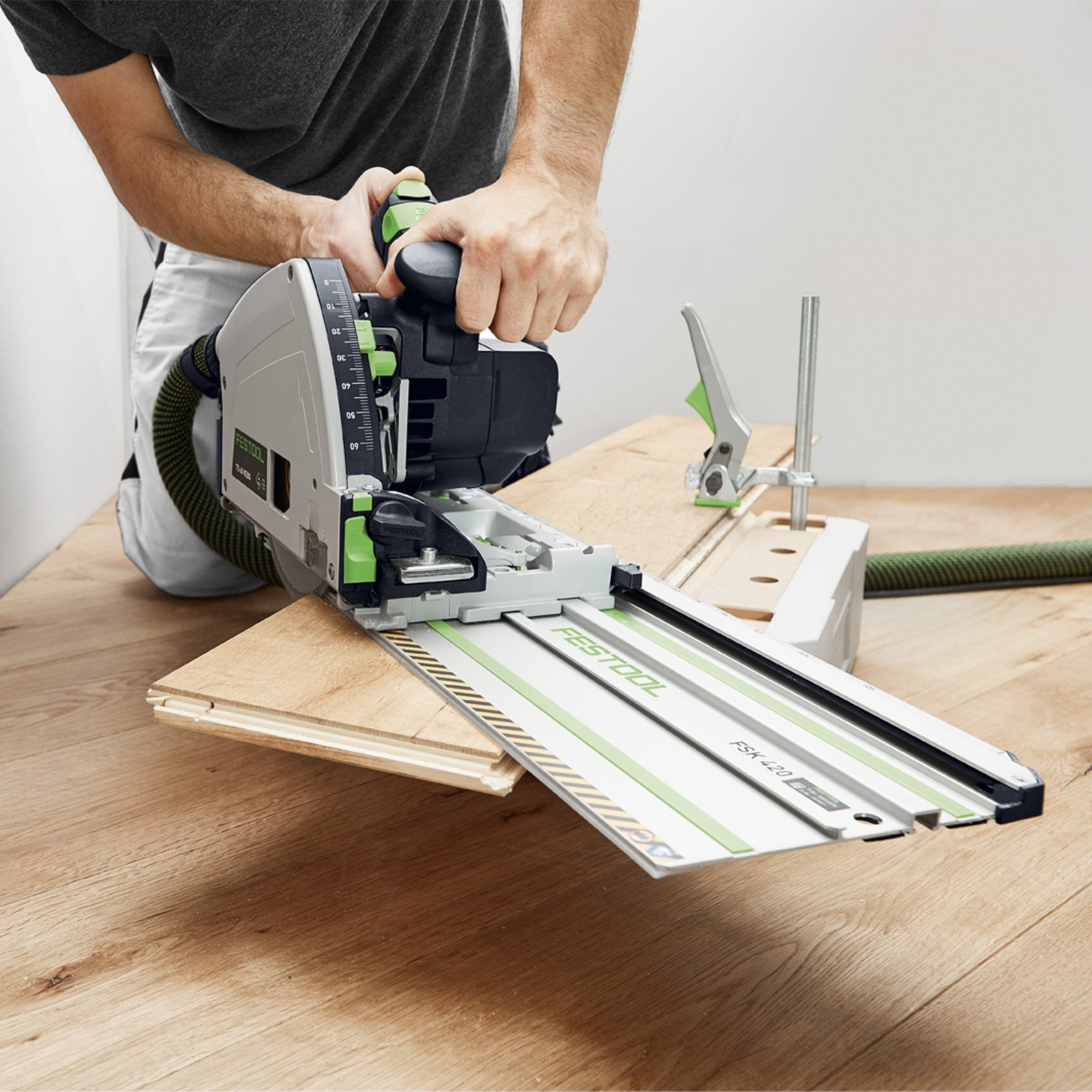 Una persona usa una sierra blanca y verde para cortar madera en una superficie de madera con una guía.