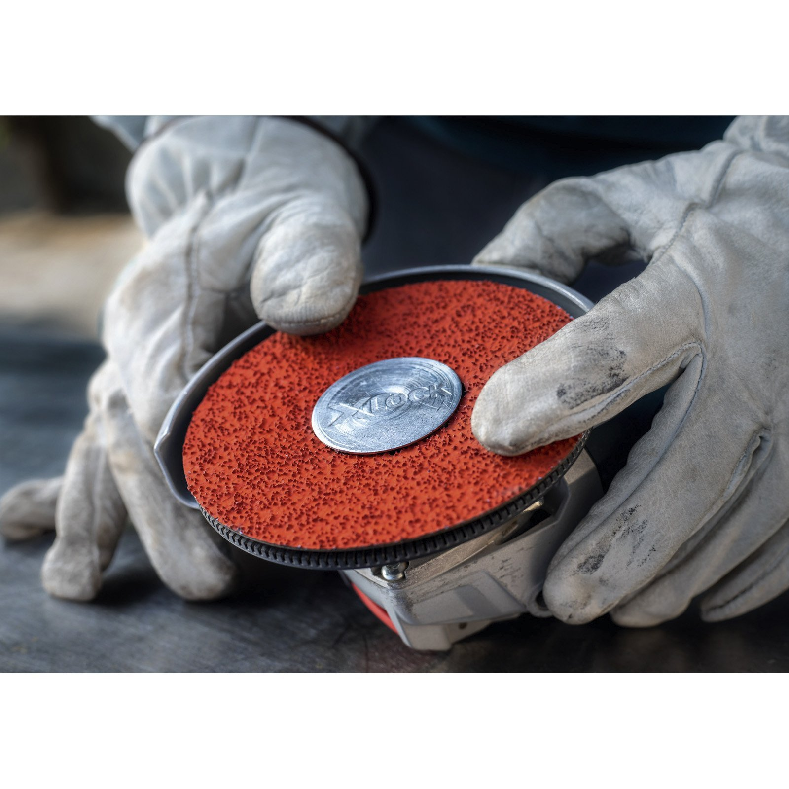 Persona con guanti tiene smerigliatrice angolare con disco rosso e blocco argento. Superficie metallica.