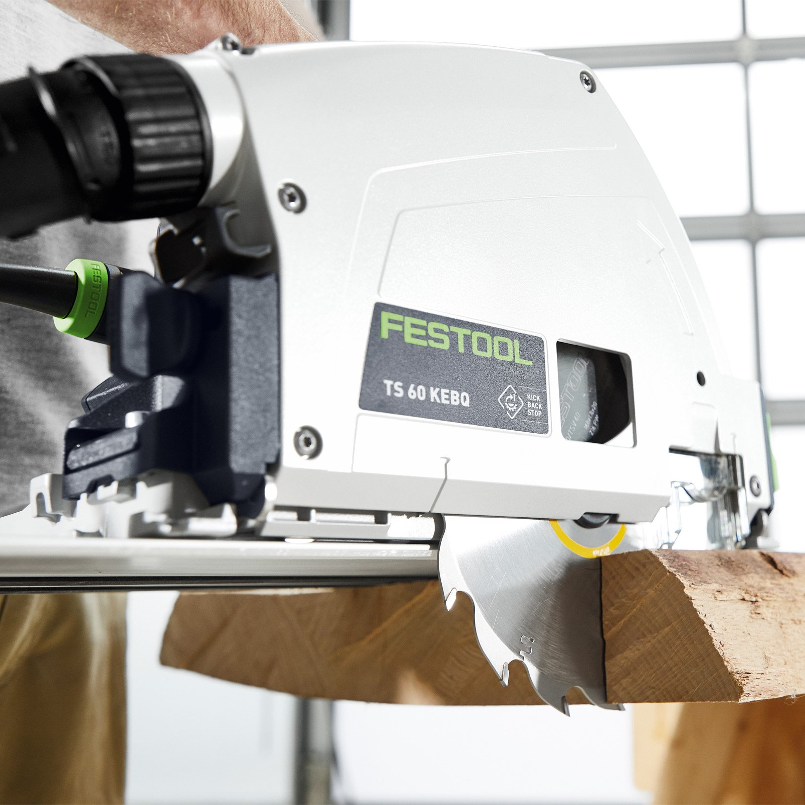 Una sierra circular Festool blanca y verde cortando madera. Se ven chispas. Una mano sostiene la herramienta.