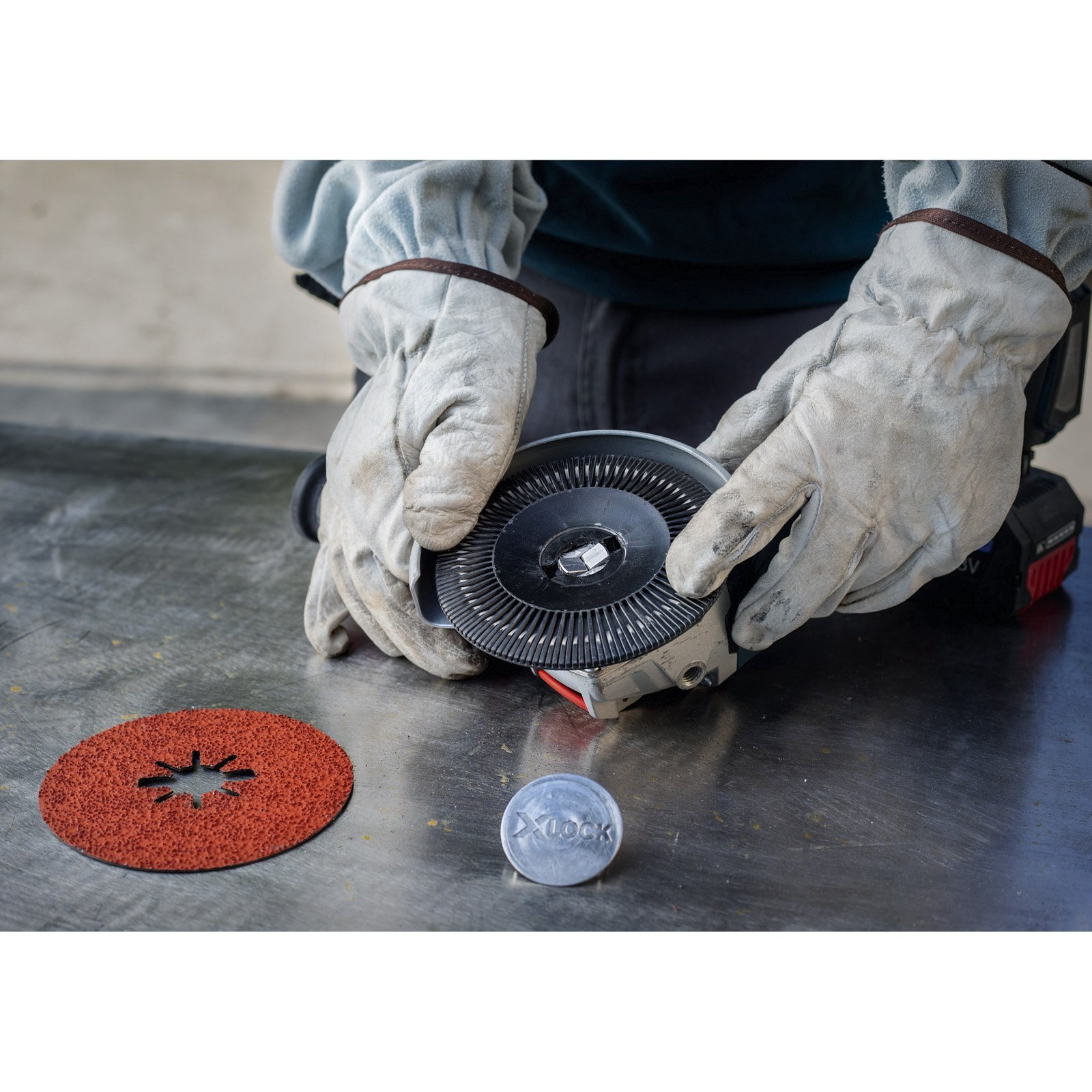 Mani con guanti tengono smerigliatrice e disco. Disco rosso e pezzo di metallo su superficie metallica.
