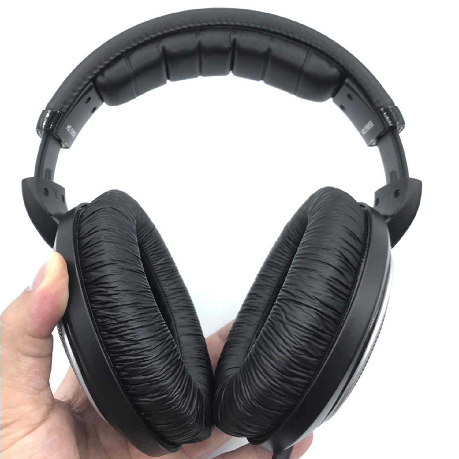 Ein Paar schwarze Kopfhörer mit großen Ohrmuscheln, gehalten von einer Hand, vor weißem Hintergrund.