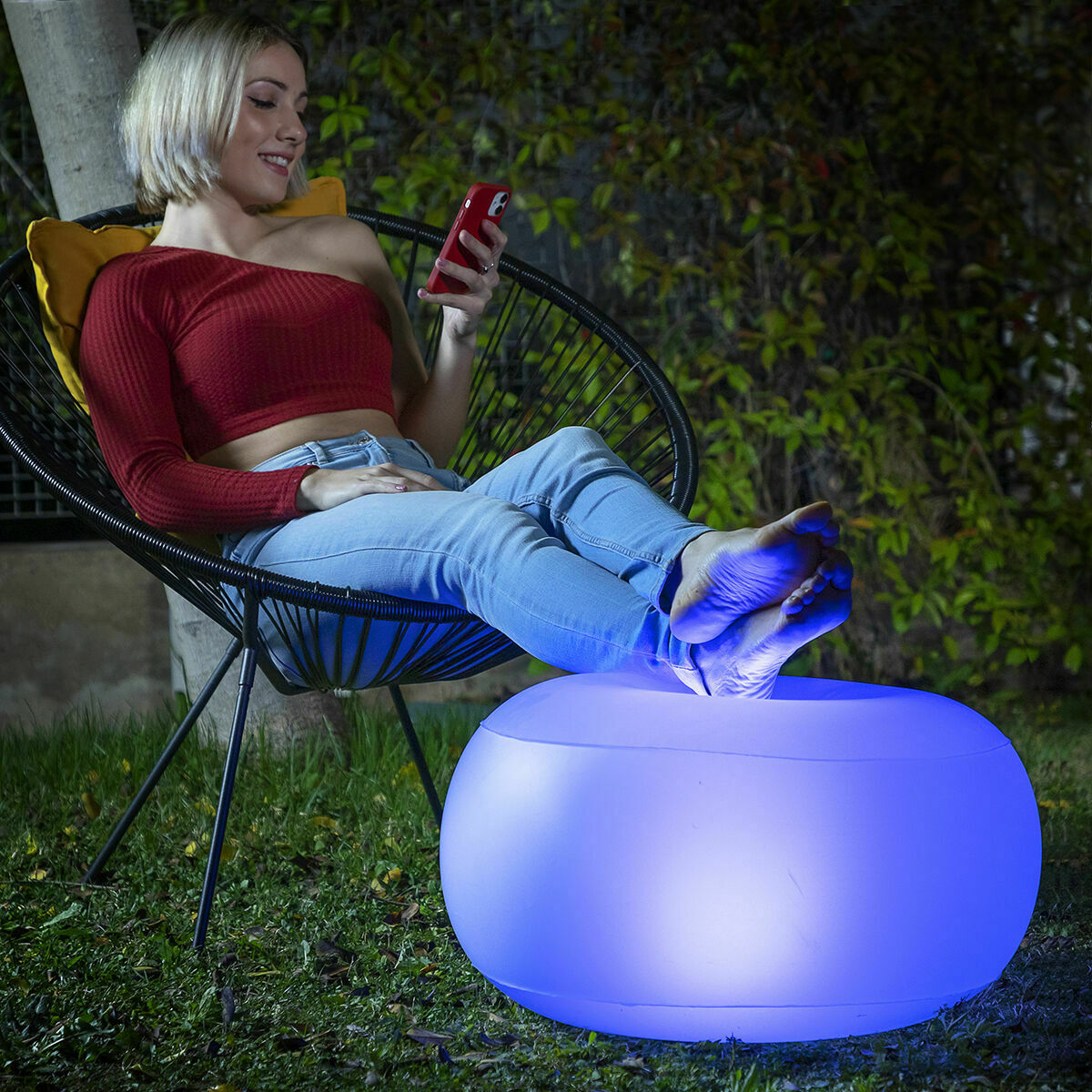 Frau am Telefon in einem Stuhl, Füße auf blau leuchtendem Hocker bei Nacht.