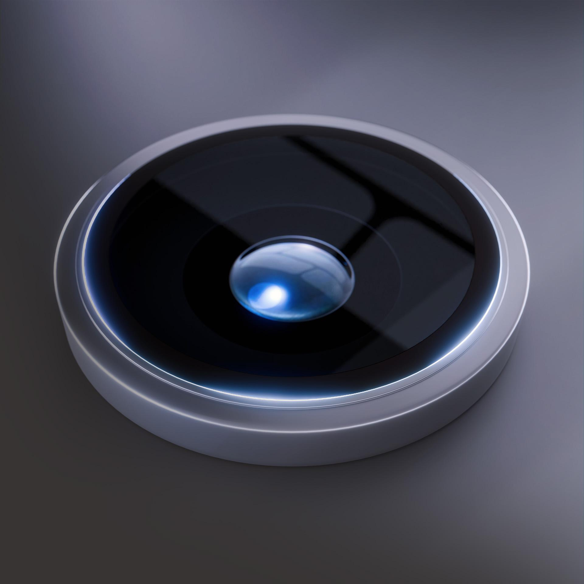 Zbliżenie obiektywu aparatu. Obiektyw jest okrągły i odblaskowy, otoczony srebrną obwódką. Niebieska poświata otacza obiektyw.