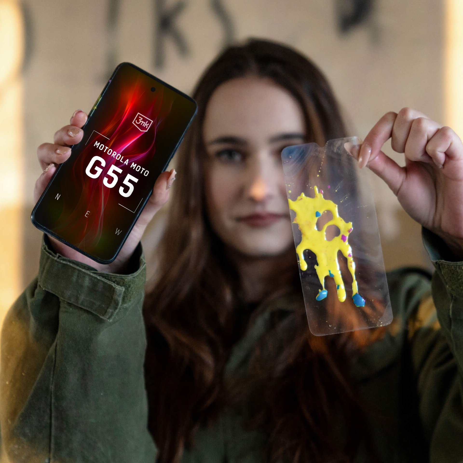 Donna che tiene in mano un telefono con display Motorola G55 e una custodia trasparente con vernice gialla.