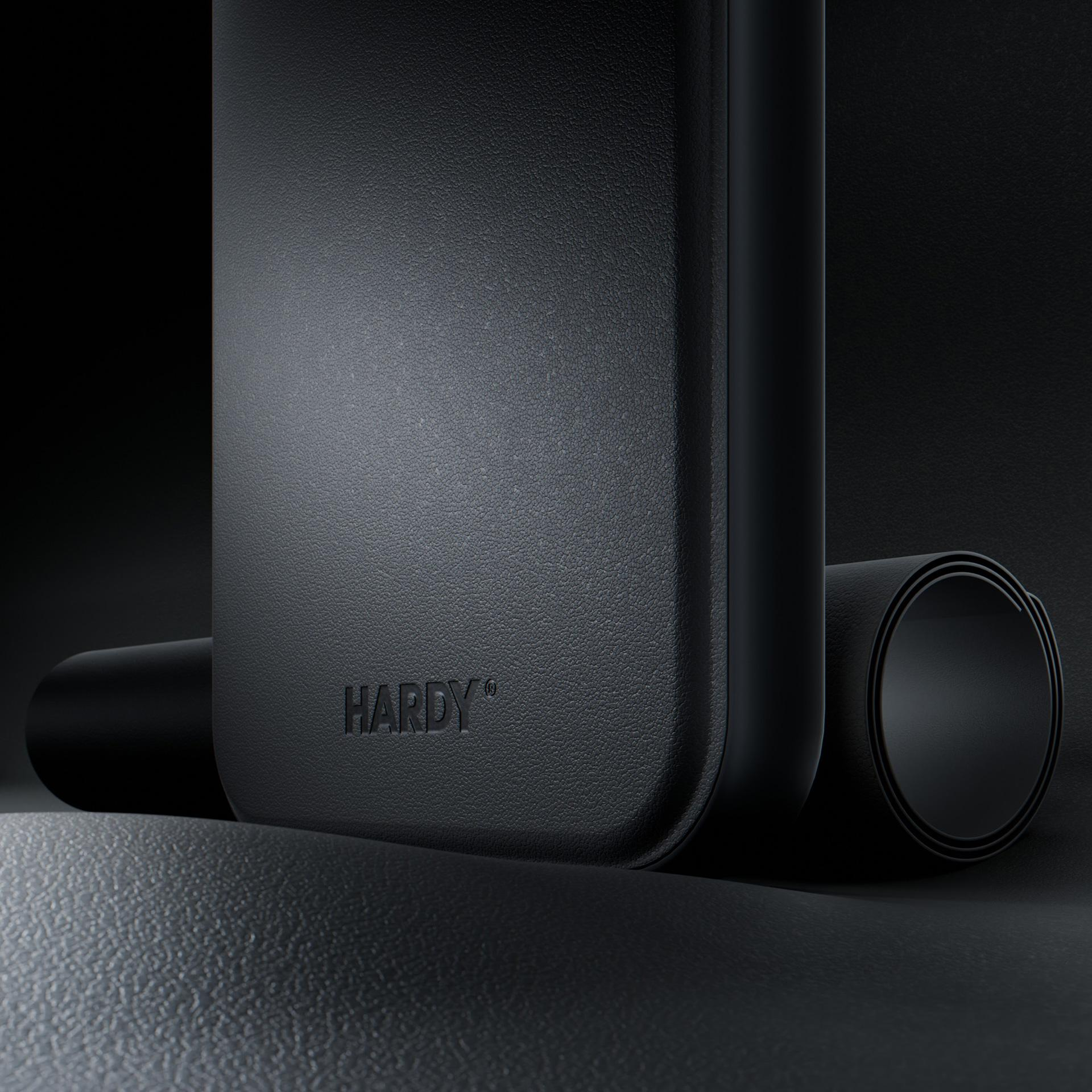 Oggetto nero con testo 'HARDY', accanto a forma arrotolata. Superficie strutturata, grigio scuro. Sfondo scuro.
