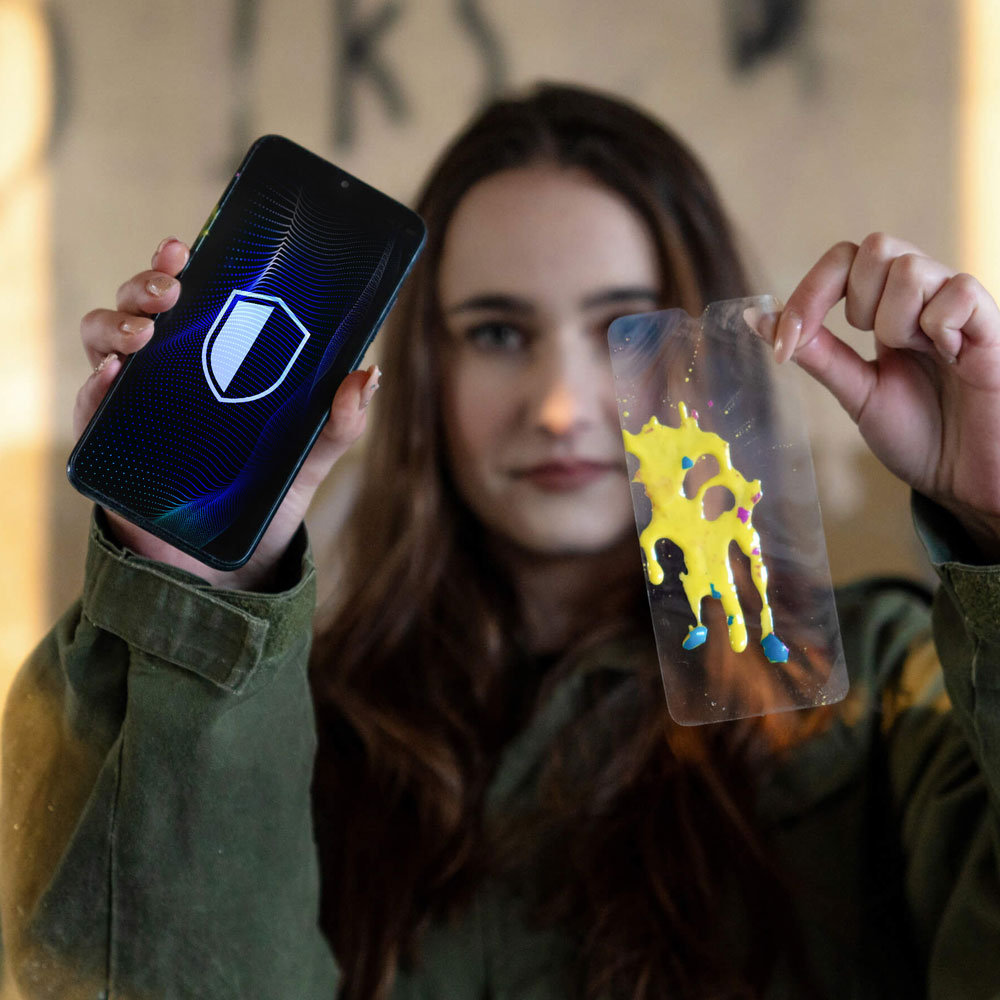 Kobieta trzymająca telefon z ikoną tarczy i plastikową osłonę z żółtą i niebieską farbą.