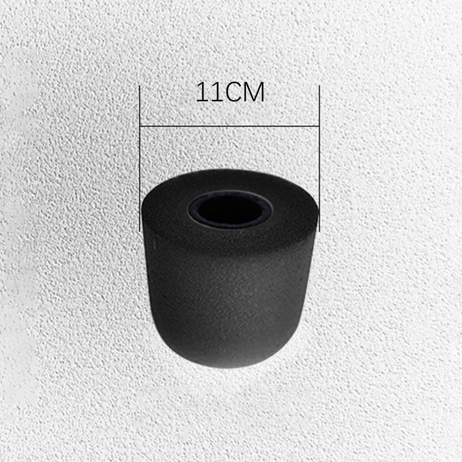 Een zwart cilindrisch object met een gat in het midden wordt getoond tegen een getextureerde witte achtergrond, met een meting van 11 cm.