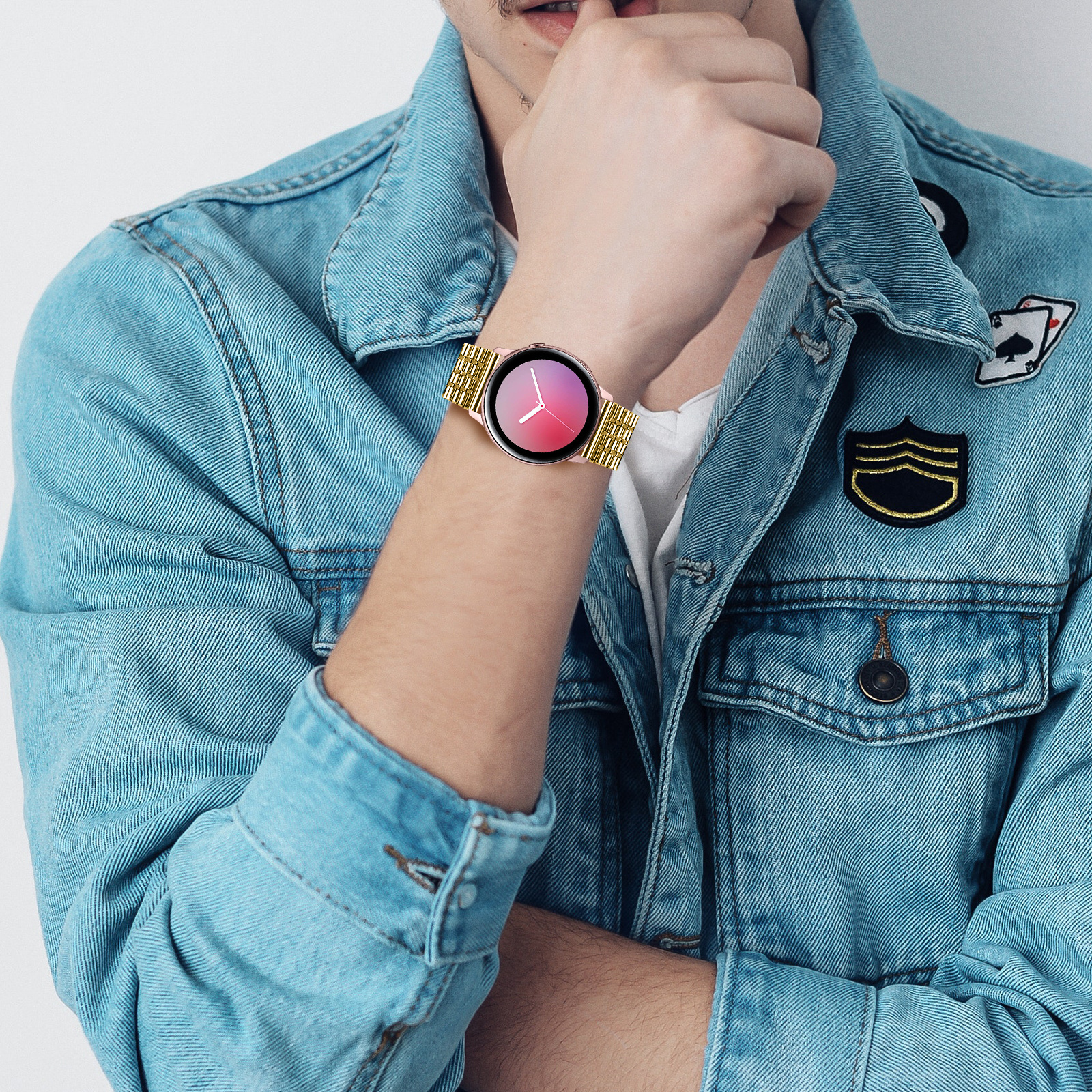 Eine Person trägt eine hellblaue Jeansjacke und eine goldene Uhr. Das Zifferblatt hat einen rosa-lila Farbverlauf.