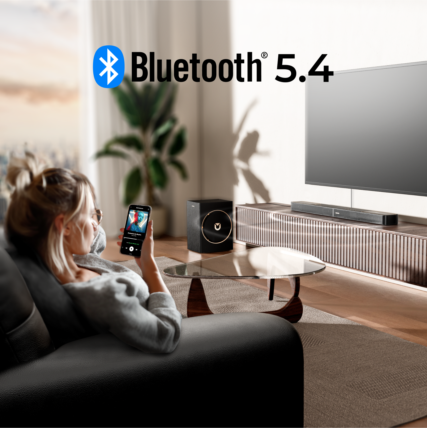 Kobieta na kanapie używa telefonu, połączonego z Bluetooth 5.4. TV i soundbar w tle. Subwoofer i stolik kawowy z przodu.