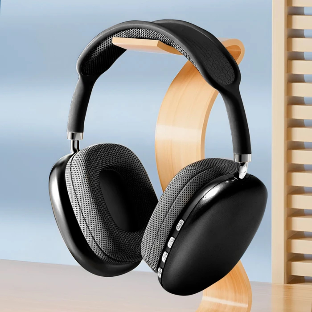 Auriculares negros con almohadillas grises sobre un soporte de madera, contra un fondo azul claro. Listones de madera a la derecha.