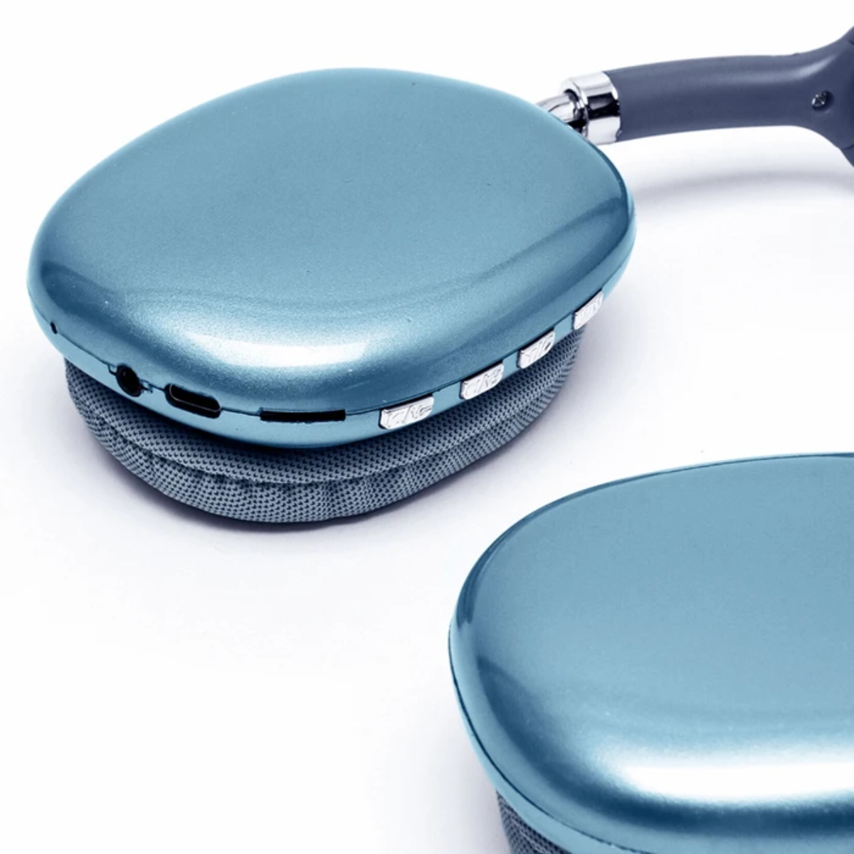 Primer plano de auriculares azules. Un auricular está enfocado, mostrando botones y puertos. Cojines de tela gris y fondo blanco.