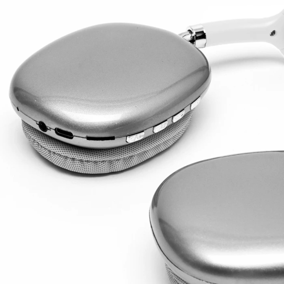 Auriculares plateados sobre fondo blanco. Un auricular enfocado, mostrando botones y puertos. El otro está desenfocado.