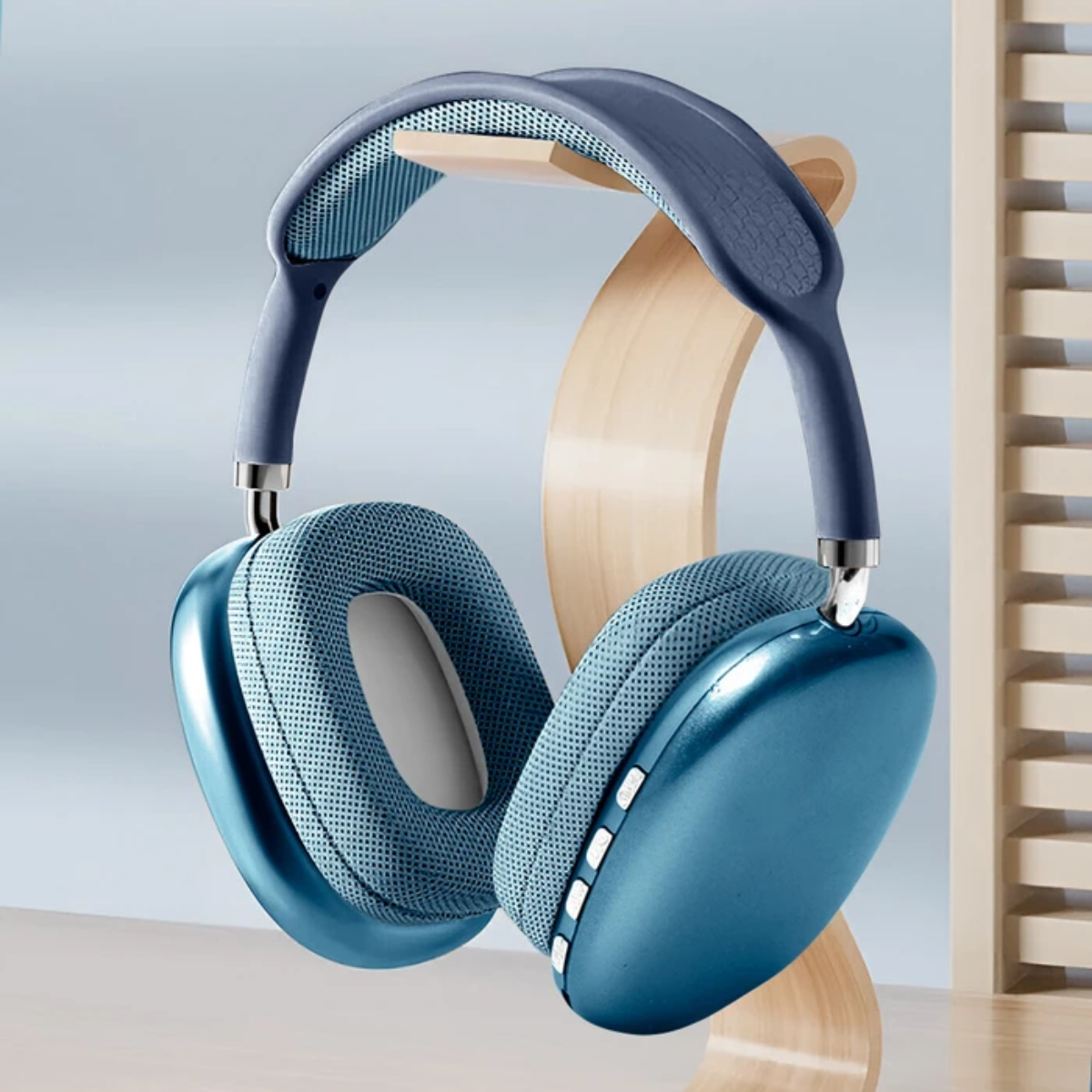 Auriculares azules sobre un soporte de madera. Los auriculares son azules con almohadillas de malla. El soporte es de madera clara. Fondo borroso.