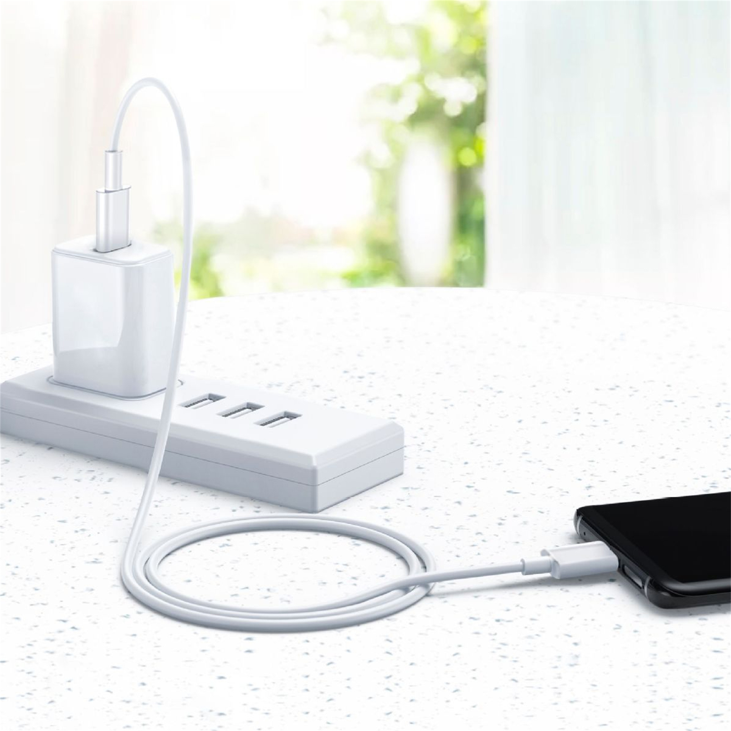 Ein weißes Ladegerät und eine Steckdosenleiste stehen auf einem Tisch. Ein Kabel verbindet das Ladegerät mit einem schwarzen Telefon.