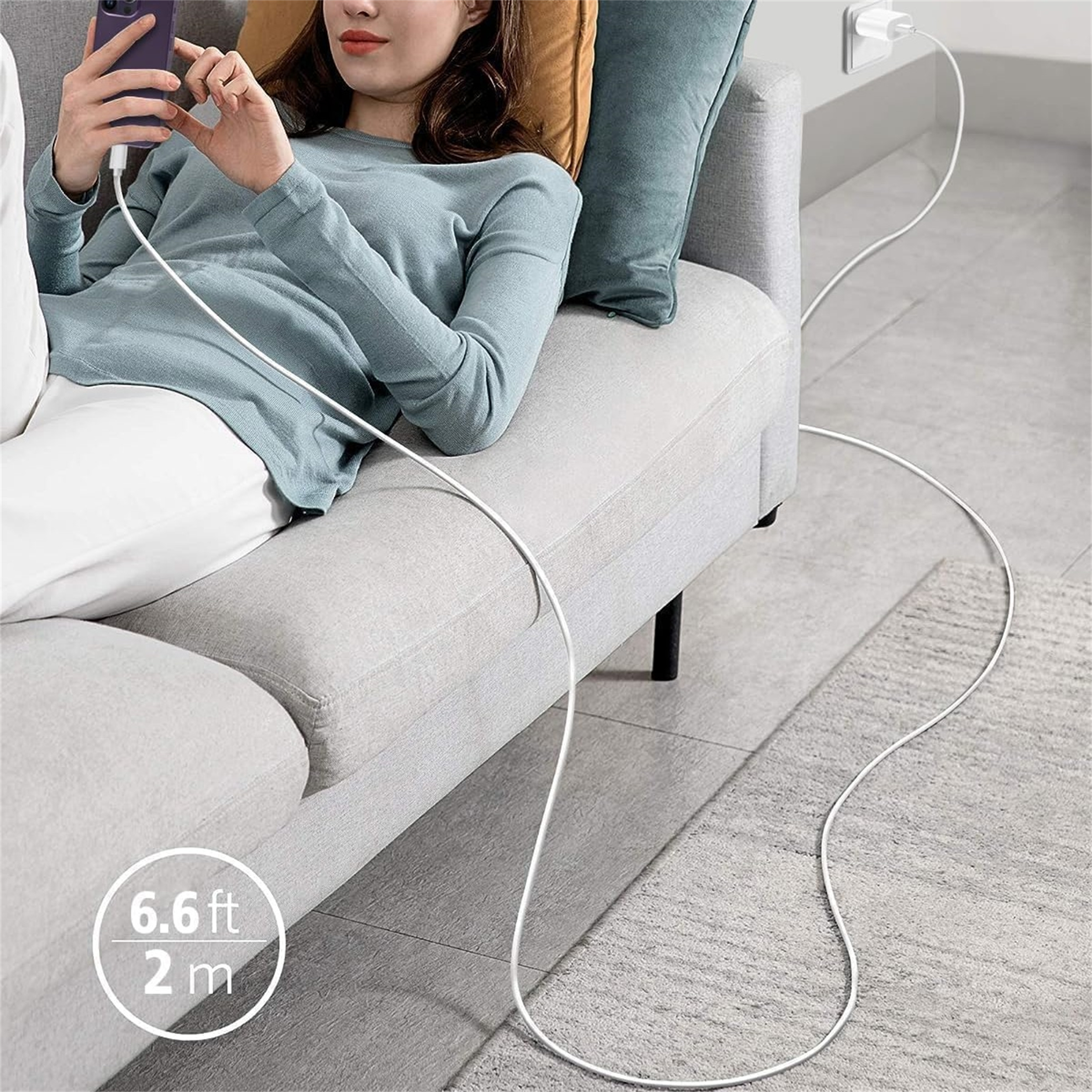 Eine Frau auf einem Sofa benutzt ein Telefon und lädt es auf. Ein weißes Kabel führt von dem Telefon zu einer Steckdose.
