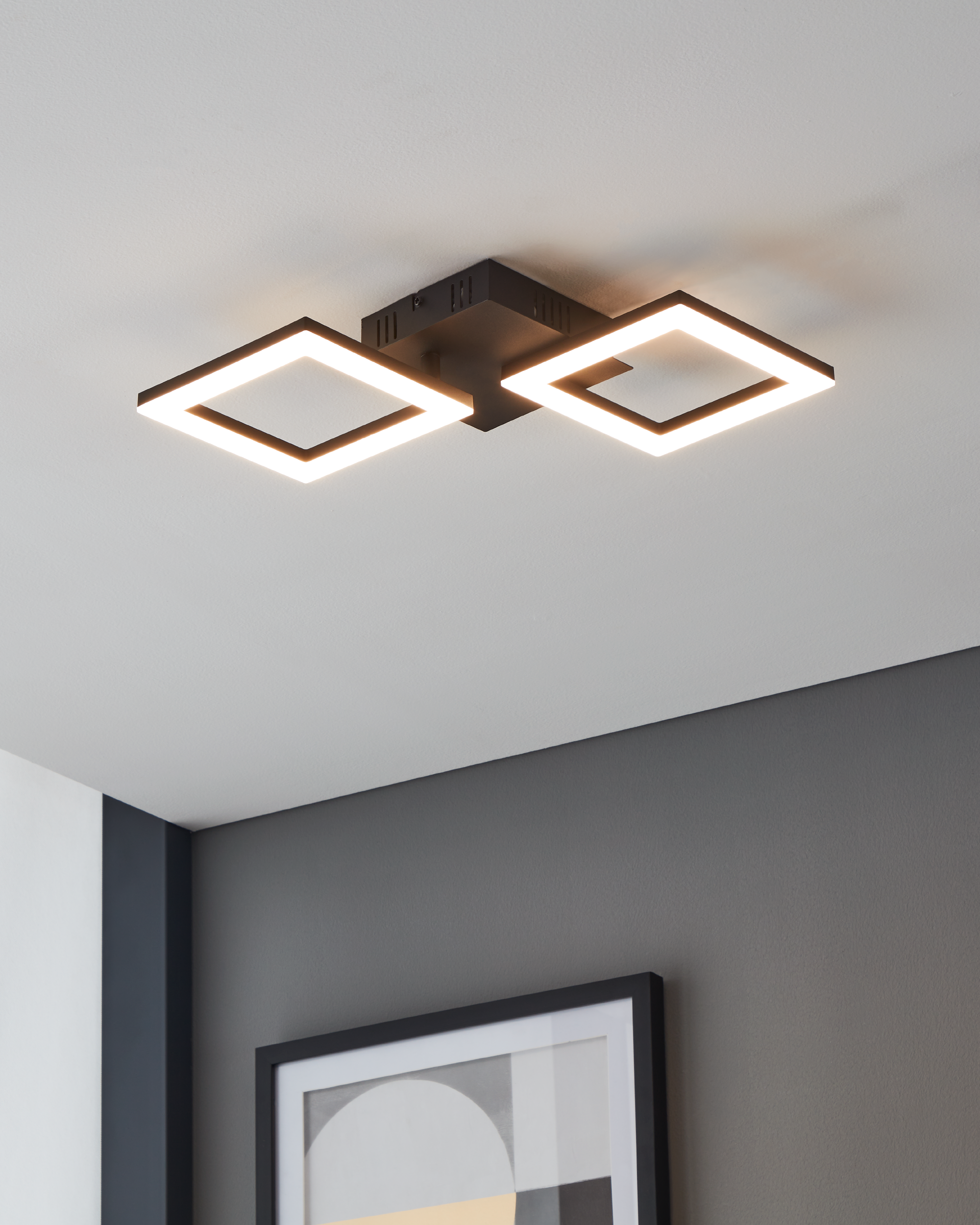 Una lampada da soffitto con due luci quadrate. Lo sfondo ha un soffitto bianco e una parete grigia.