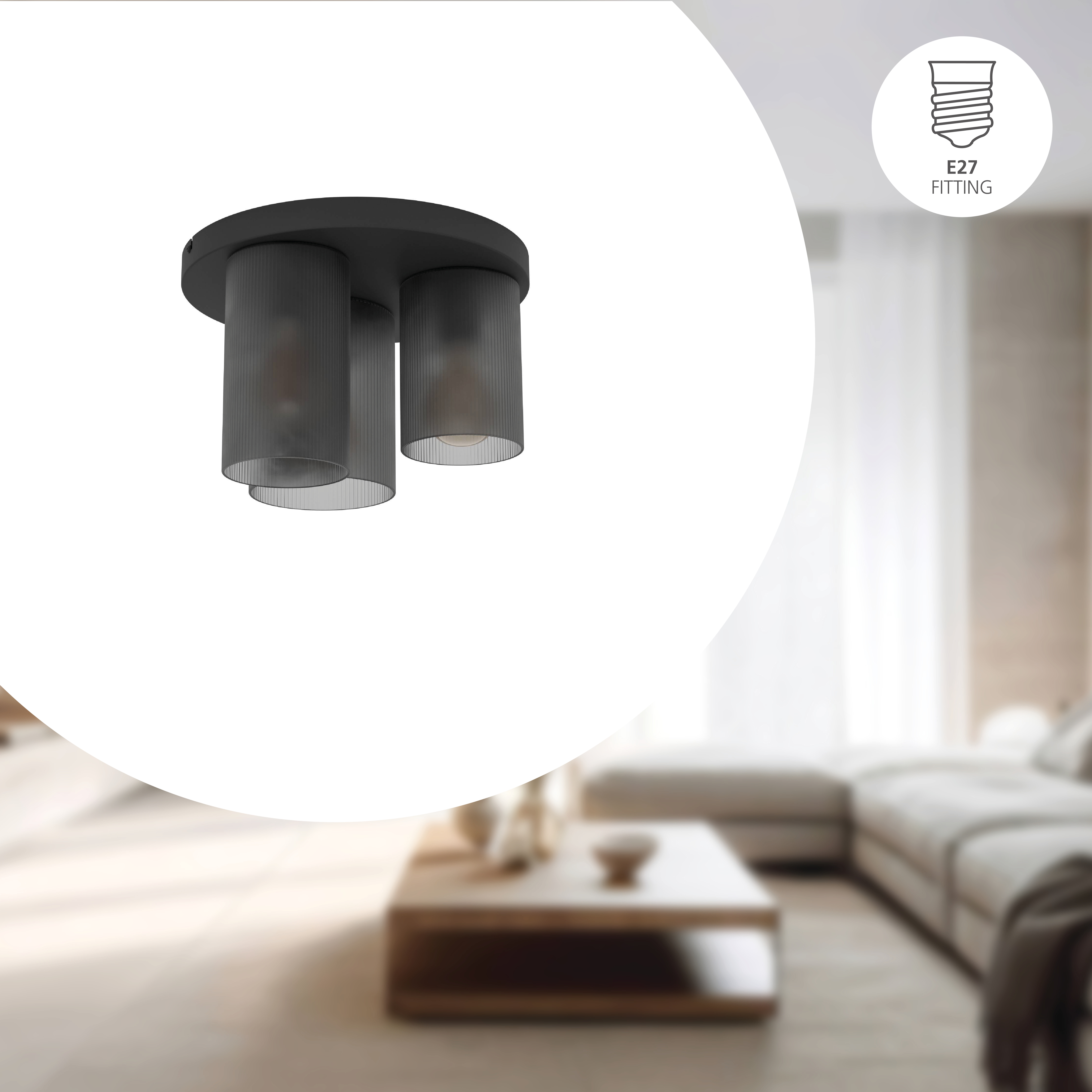 Lampada da soffitto nera con tre paralumi cilindrici. Una stanza con divano e tavolo sullo sfondo.