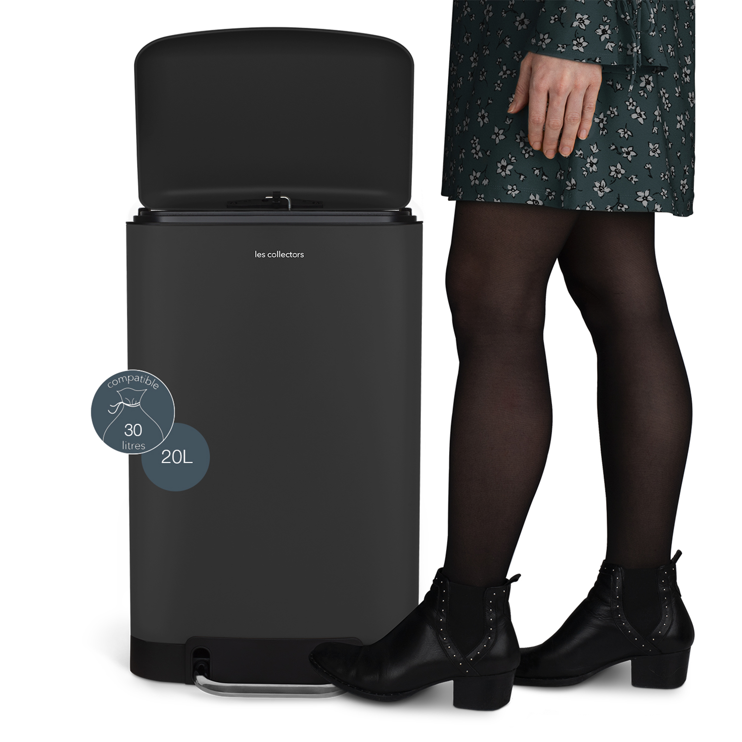 Una persona junto a un cubo de basura negro con la tapa abierta. La persona lleva un vestido floral, medias negras y botas.