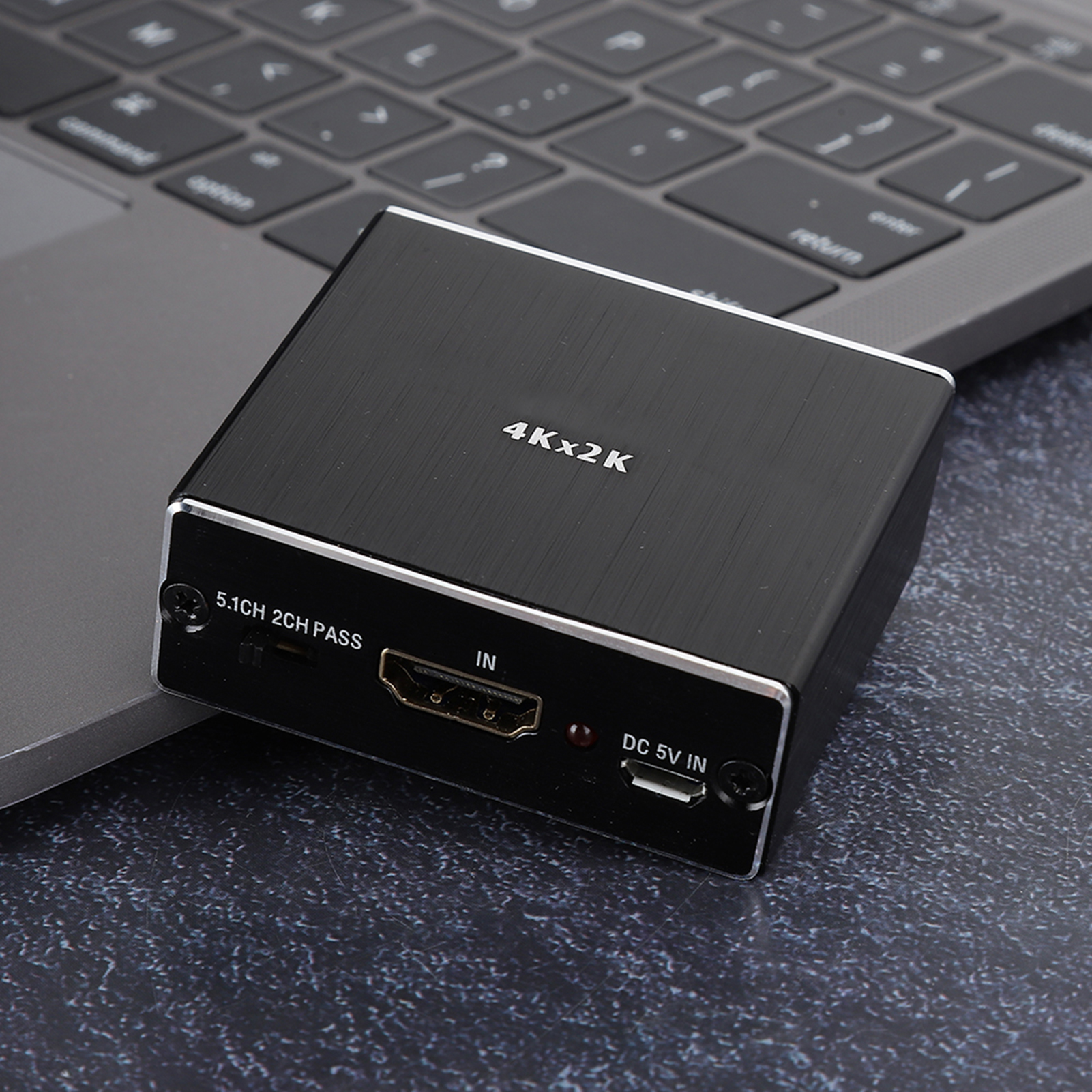 Ein schwarzer HDMI-Adapter liegt auf einem Laptop. Er enthält Text wie 4Kx2K, 5.1CH 2CH PASS, IN und DC 5V IN.