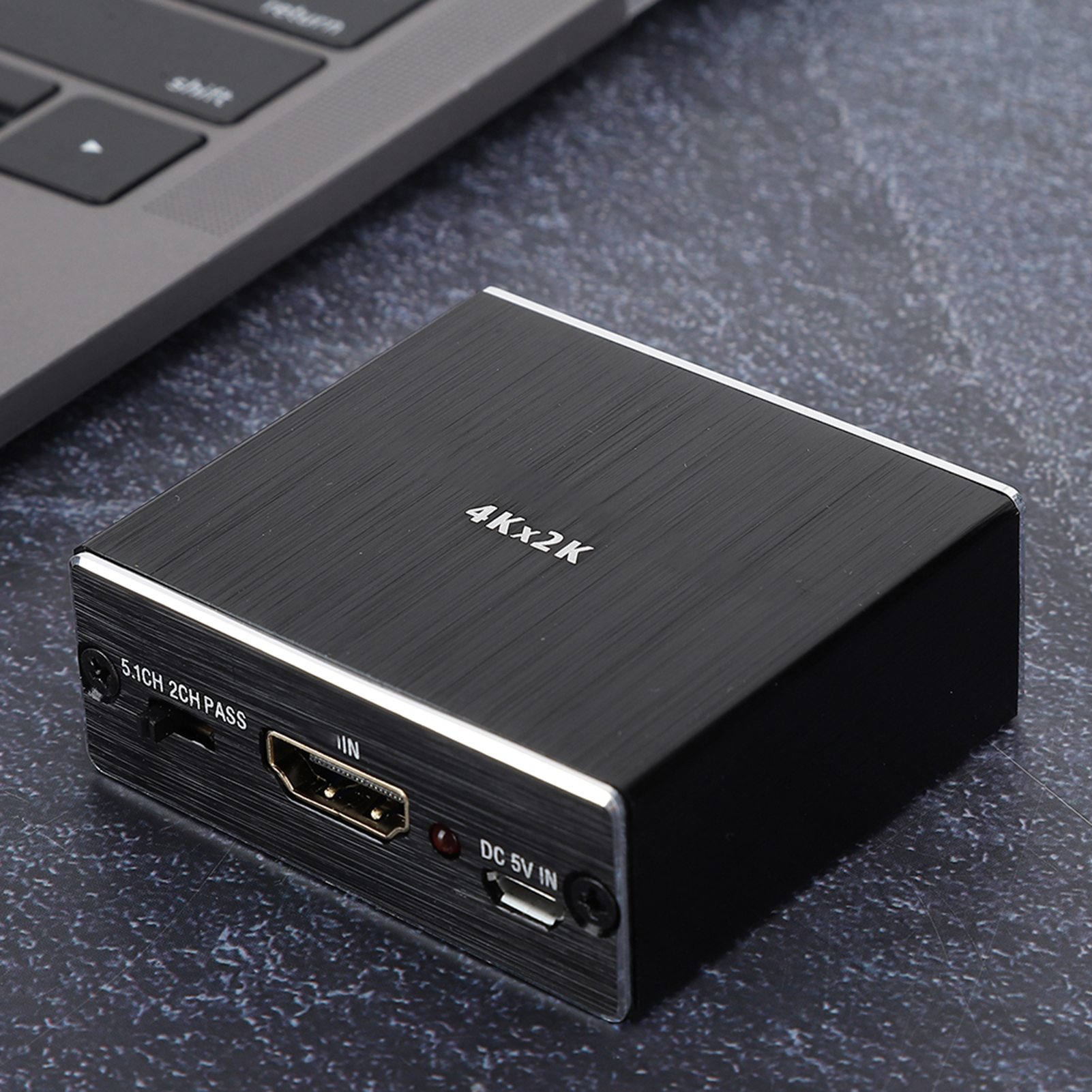 Schwarzer HDMI-Switch-Box mit silberner Einfassung auf strukturierter Oberfläche. Eine Laptop-Tastatur ist im Hintergrund.