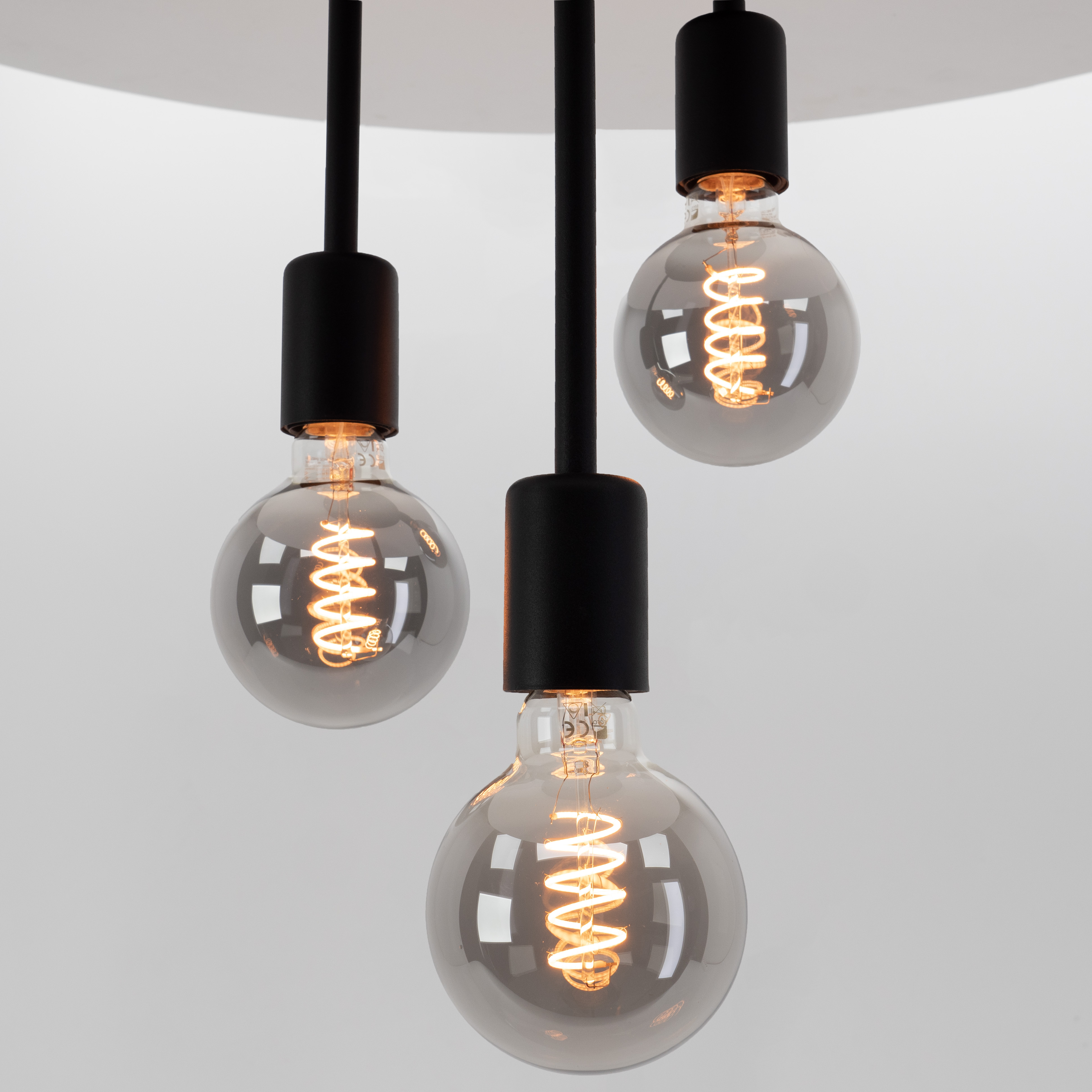 Tres lámparas colgantes con cables negros y bombillas esféricas grises ahumadas. La luz cálida brilla desde los filamentos.