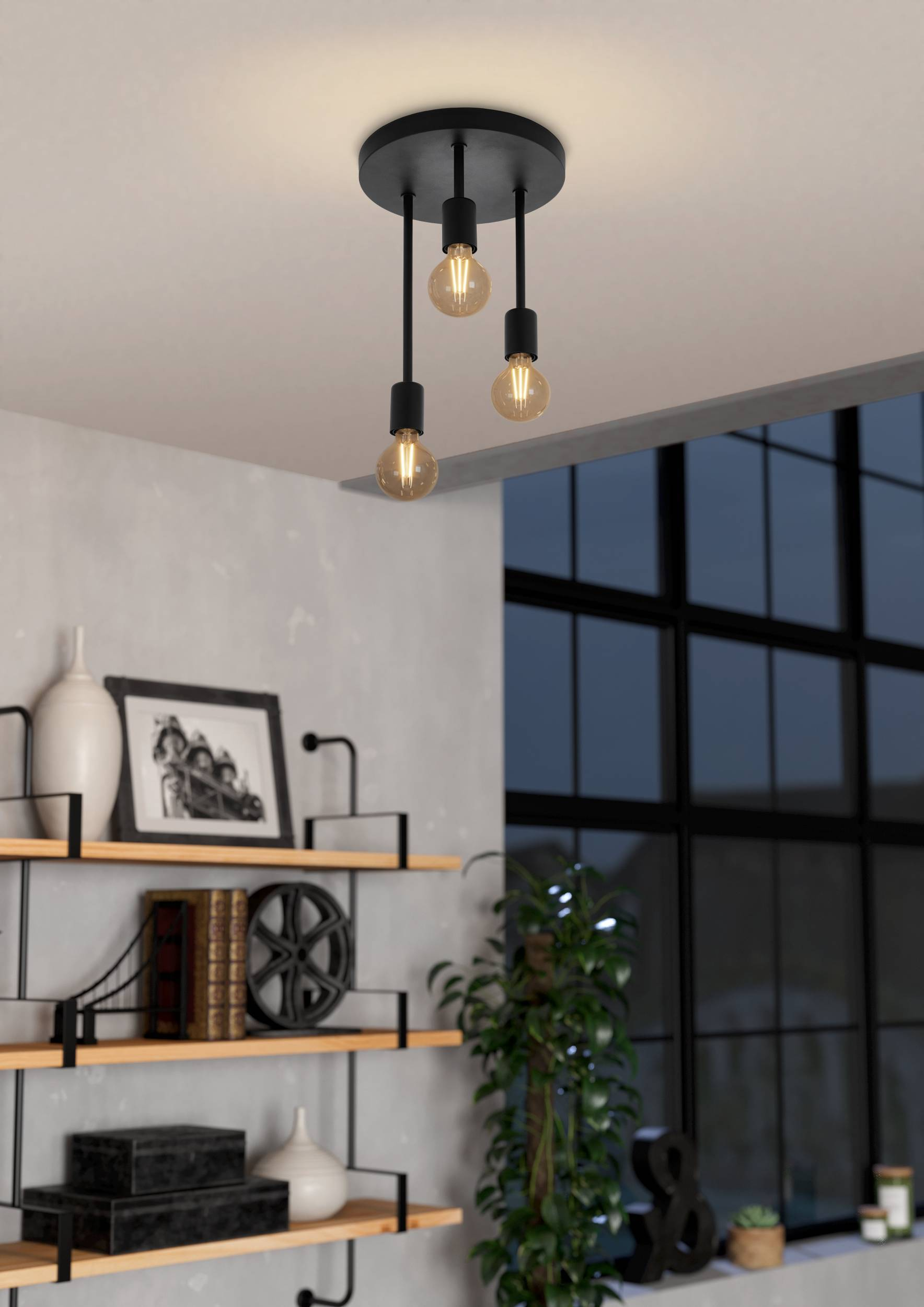 Lámpara de techo moderna con tres bombillas colgantes. Debajo hay estantes con decoración, una ventana y una planta.