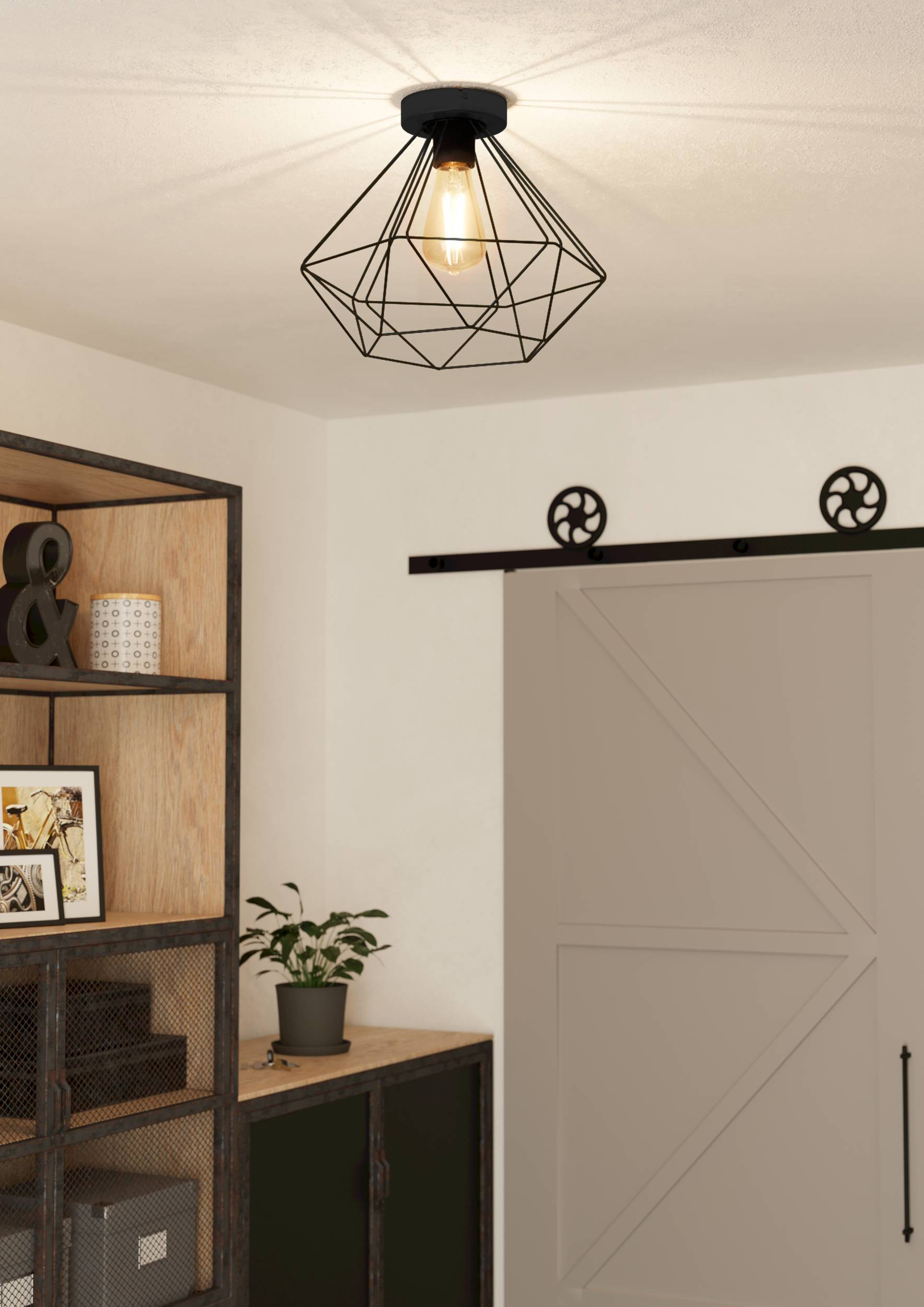 Eine schwarze geometrische Deckenlampe hängt. Ein Regal mit Dekor und eine Tür mit schwarzer Hardware sind rechts.