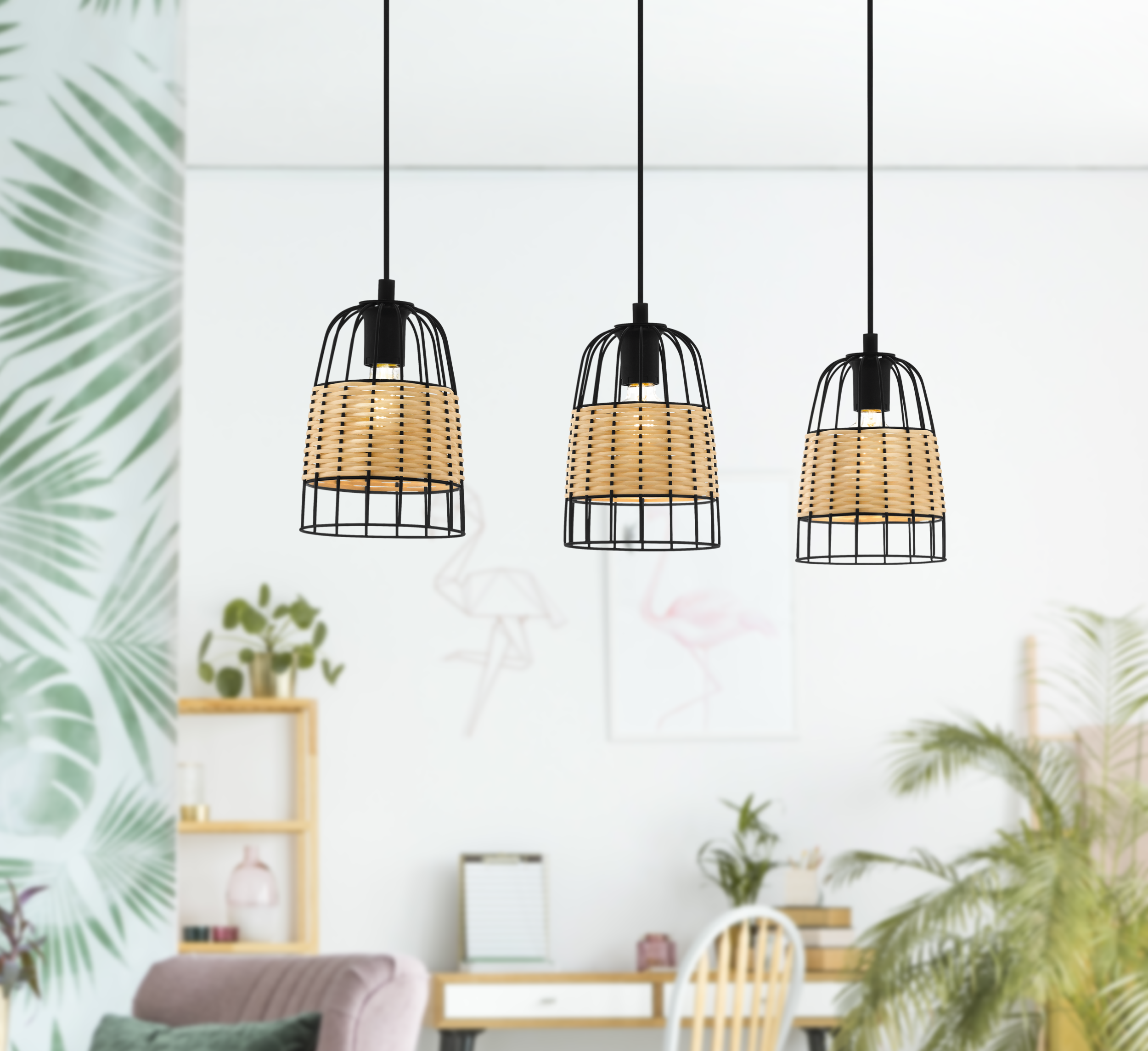 Tres lámparas colgantes con pantallas de mimbre cuelgan en una habitación. Una pared tiene un diseño de hojas, un escritorio y plantas en el fondo.