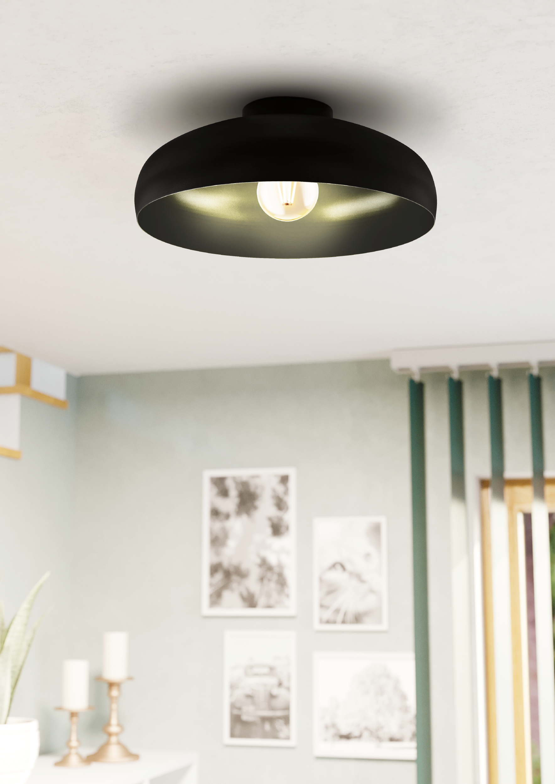 Una lampada da soffitto nera con una lampadina è centrata. Lo sfondo mostra una parete verde chiaro con immagini e una finestra.