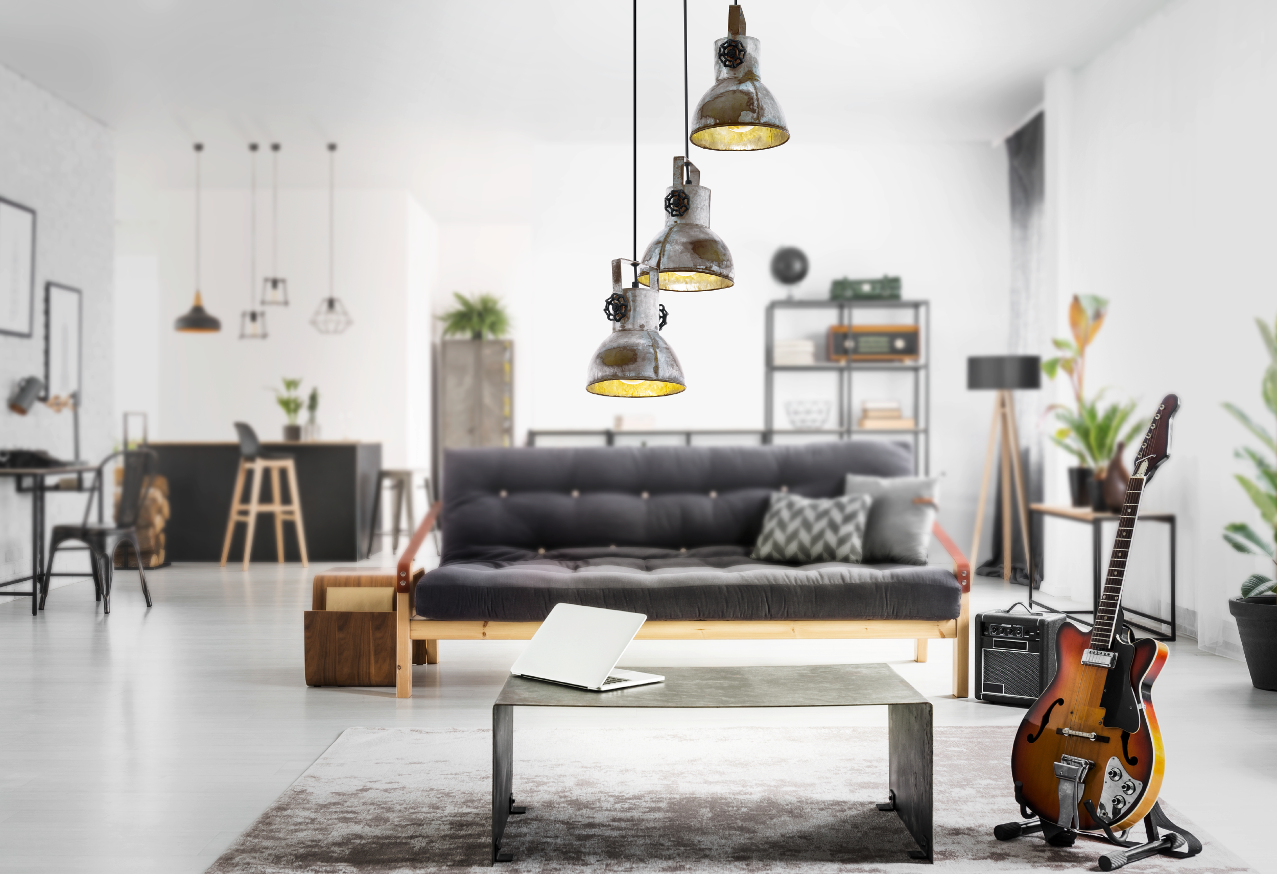 Wohnzimmer mit Futon, Gitarre und Industrie-Pendelleuchten. Ein Laptop auf dem Tisch. Der Raum ist hell und modern.