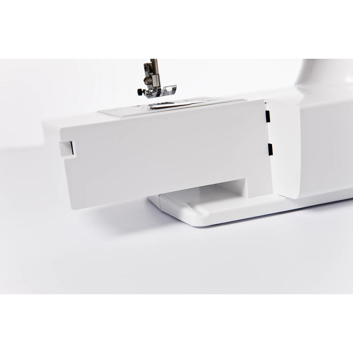 Zbliżenie białej maszyny do szycia. Widoczna igła i stopka dociskowa. Podstawa ma małą szufladę.