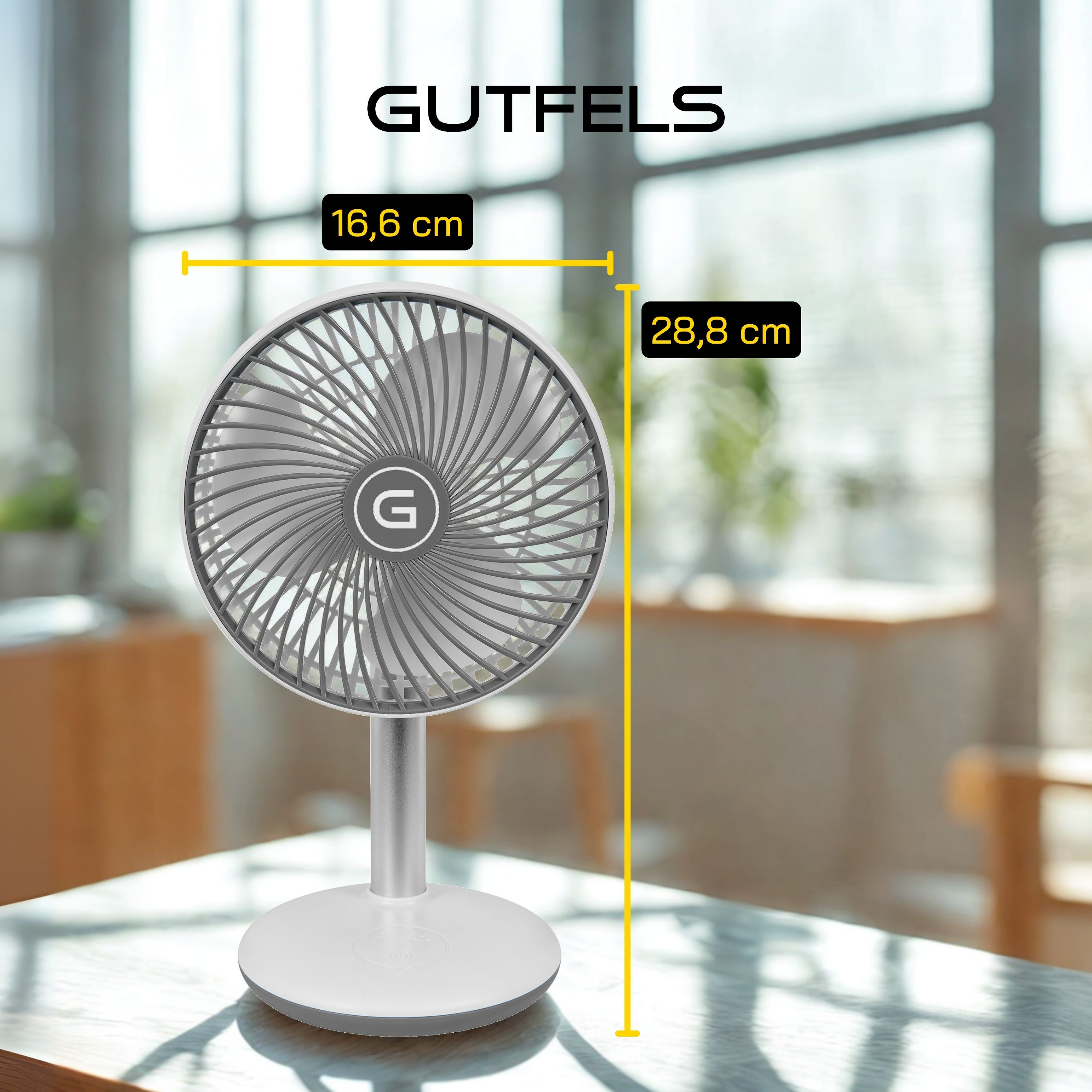 Un ventilador de escritorio blanco y gris con dimensiones etiquetadas. El fondo muestra una ventana y una mesa.