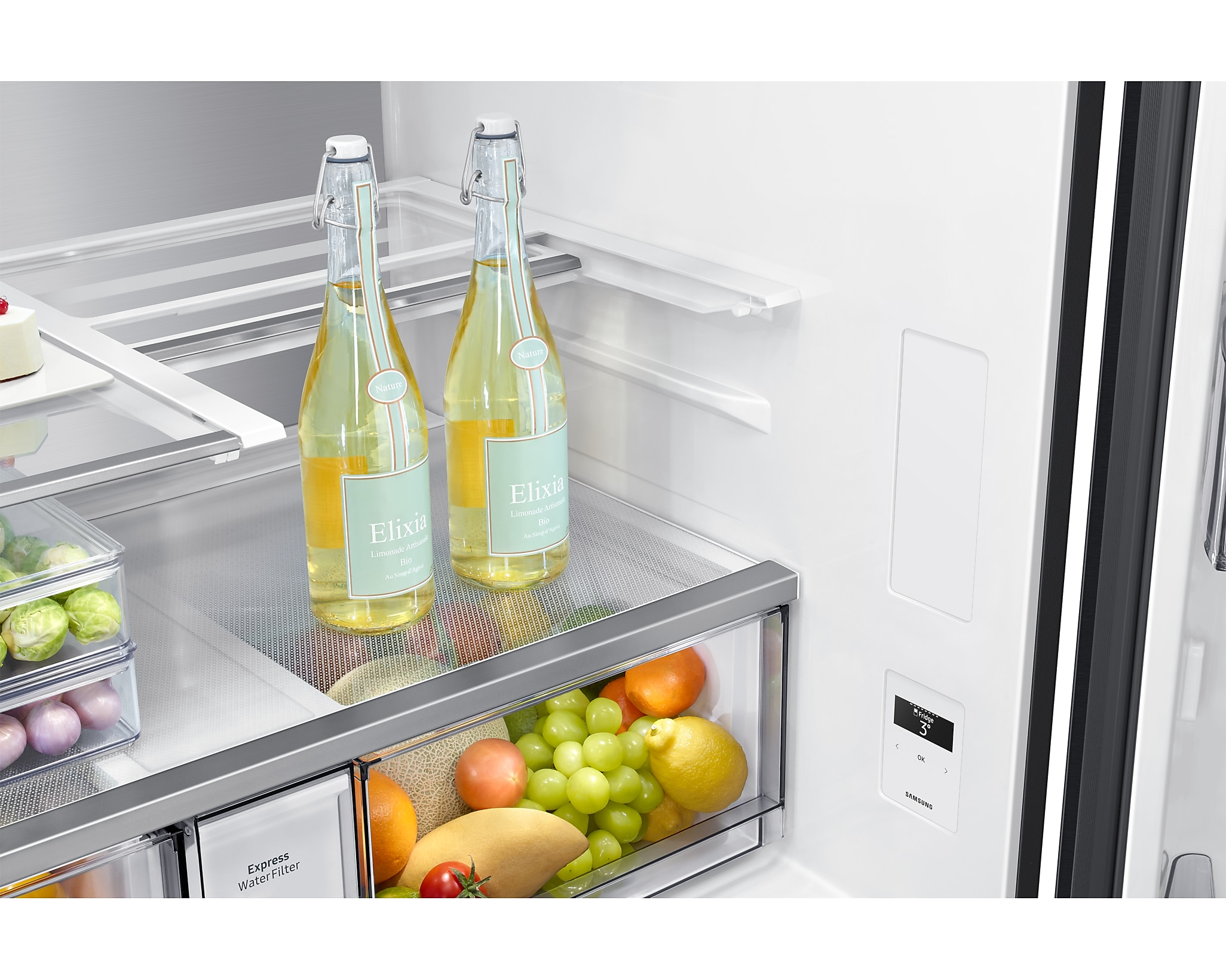 Wnętrze lodówki ze szklanymi półkami, butelkami, owocami i wyświetlaczem. Drzwi otwarte.