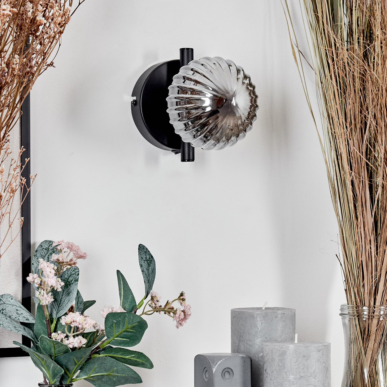Eine Wandleuchte mit geripptem Glaskolben. Die Lampe hat einen schwarzen, kreisförmigen Sockel und einen Metallarm.