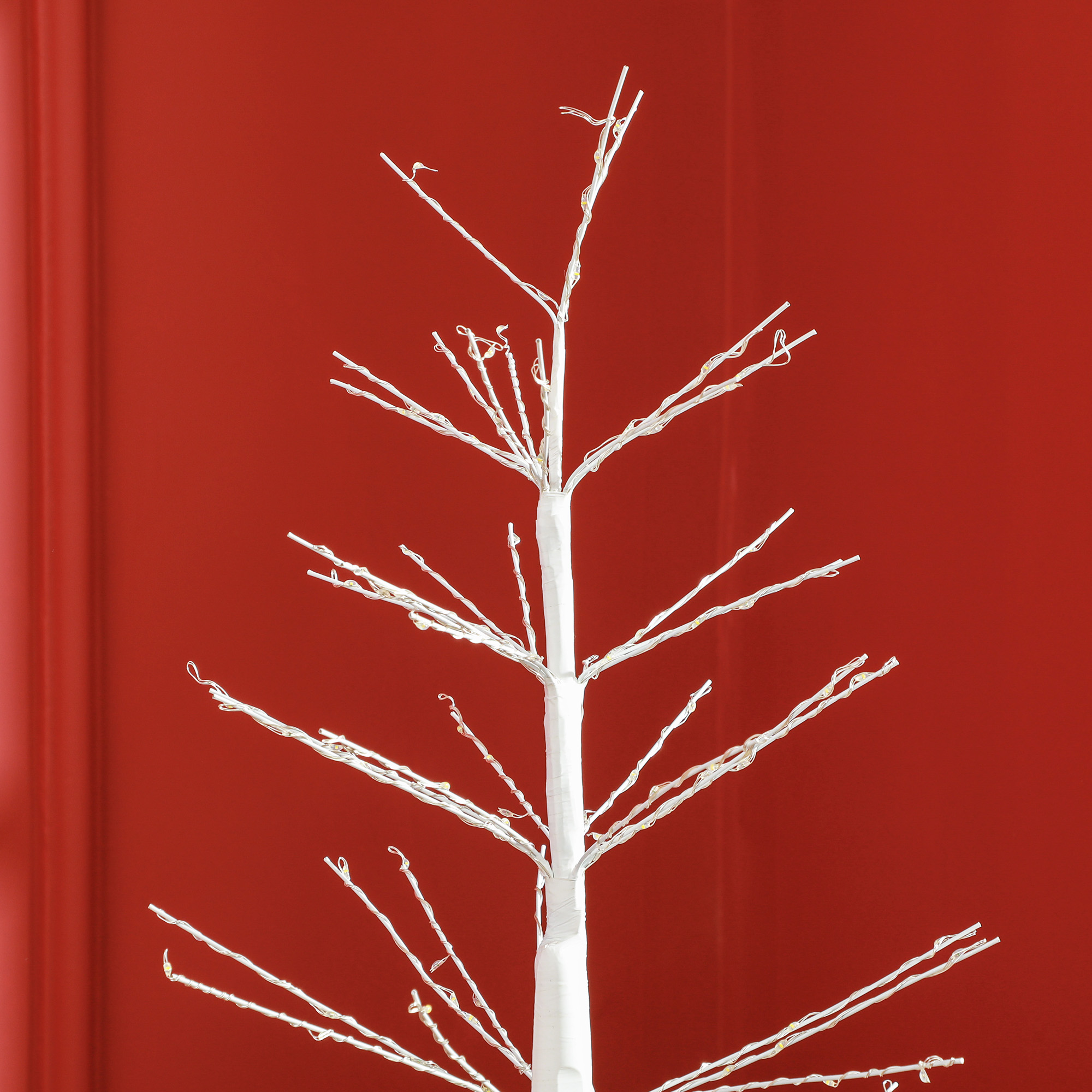 Ein weißer dekorativer Baum mit Lichtern auf rotem Hintergrund. Eine festliche Szene.