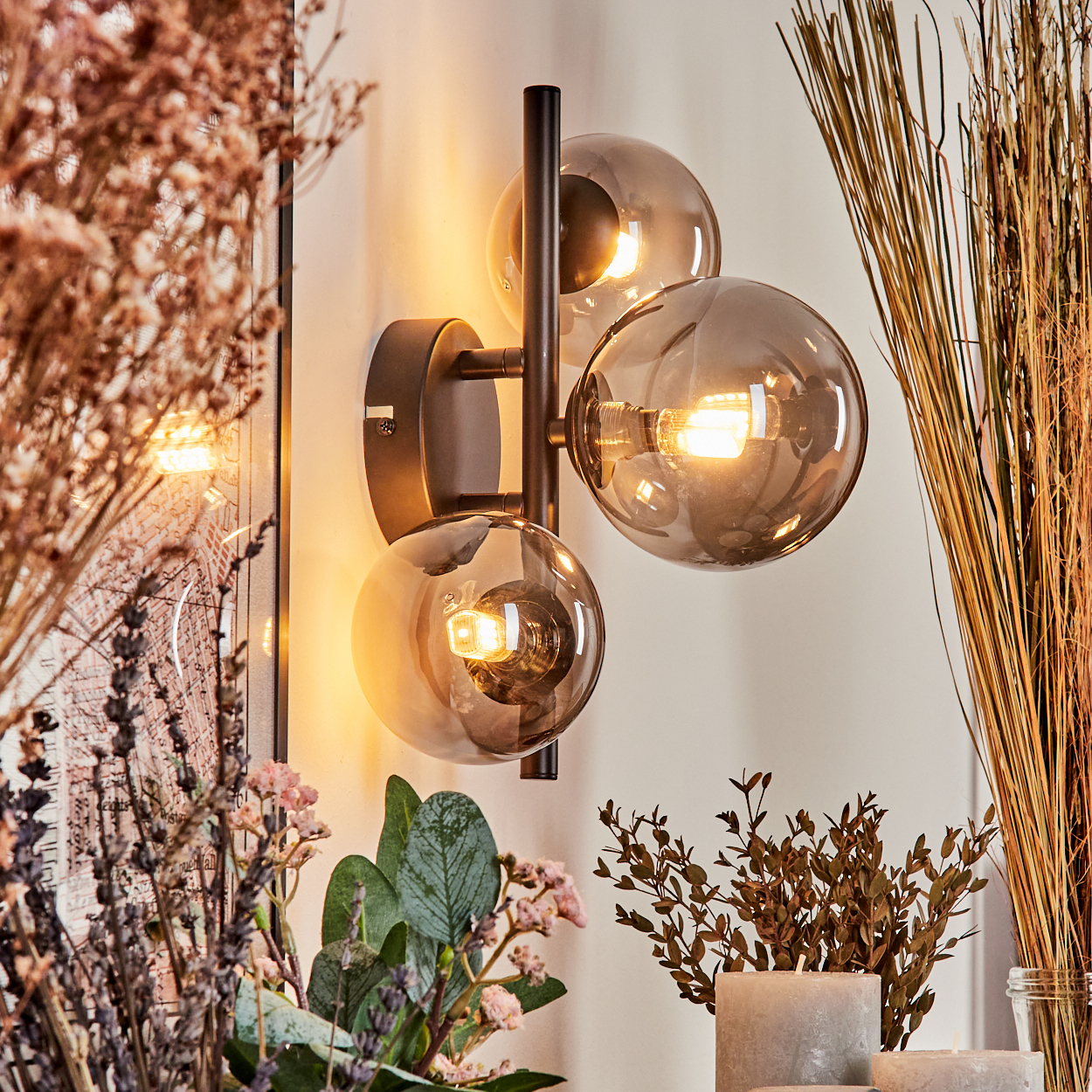 Schwarze Wandlampe mit drei runden, rauchfarbenen Glühbirnen, mit Pflanzen.