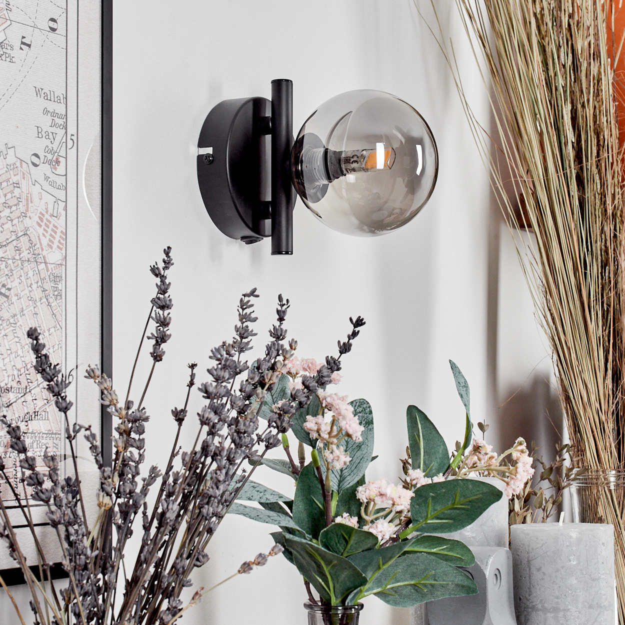 Schwarze Wandlampe mit einer Kugel aus Rauchglas. Trockenblumen und eine Karte im Hintergrund.