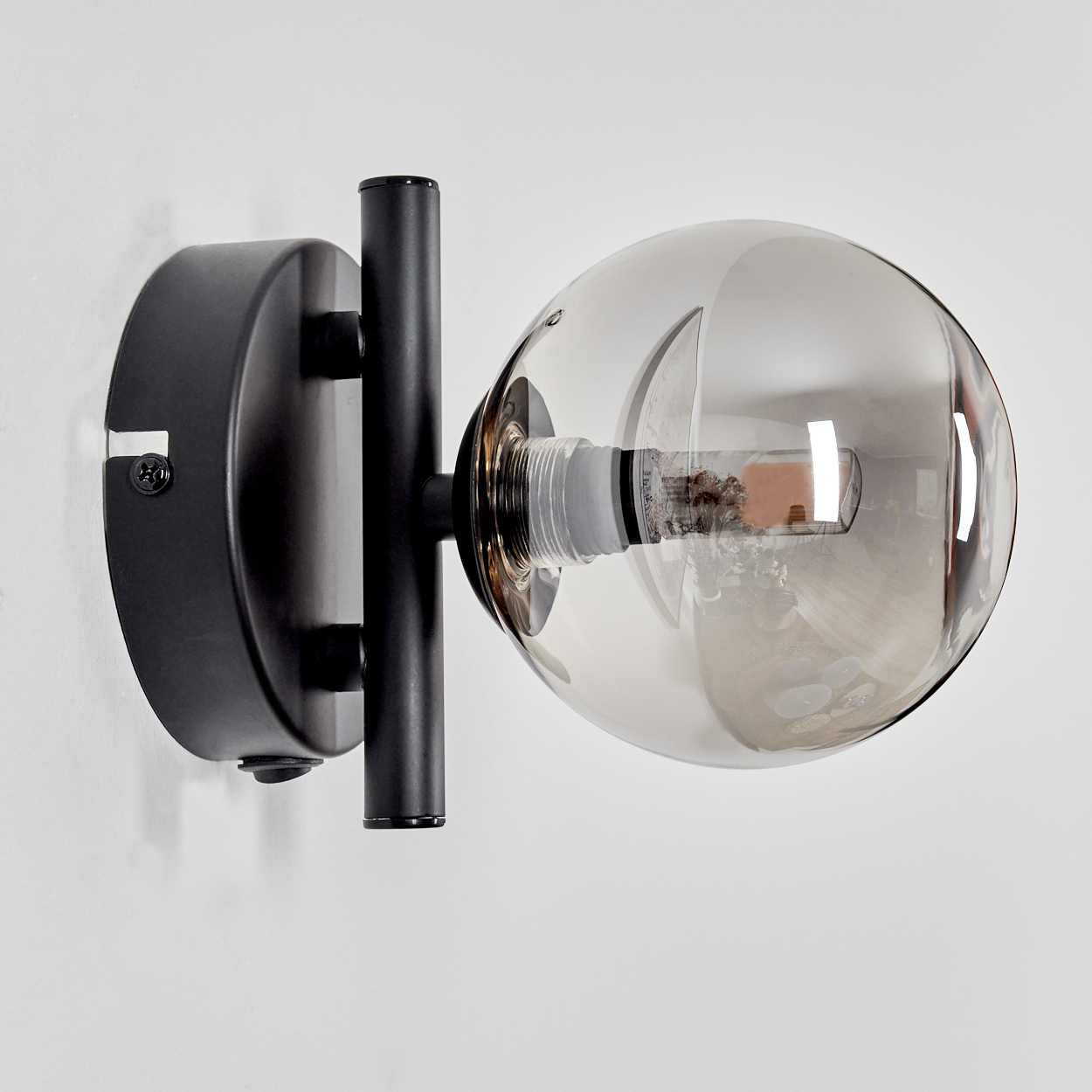 Schwarze Wandlampe mit einer Rauchglaskugel. Die Lampe ist an einer weißen Wand montiert.