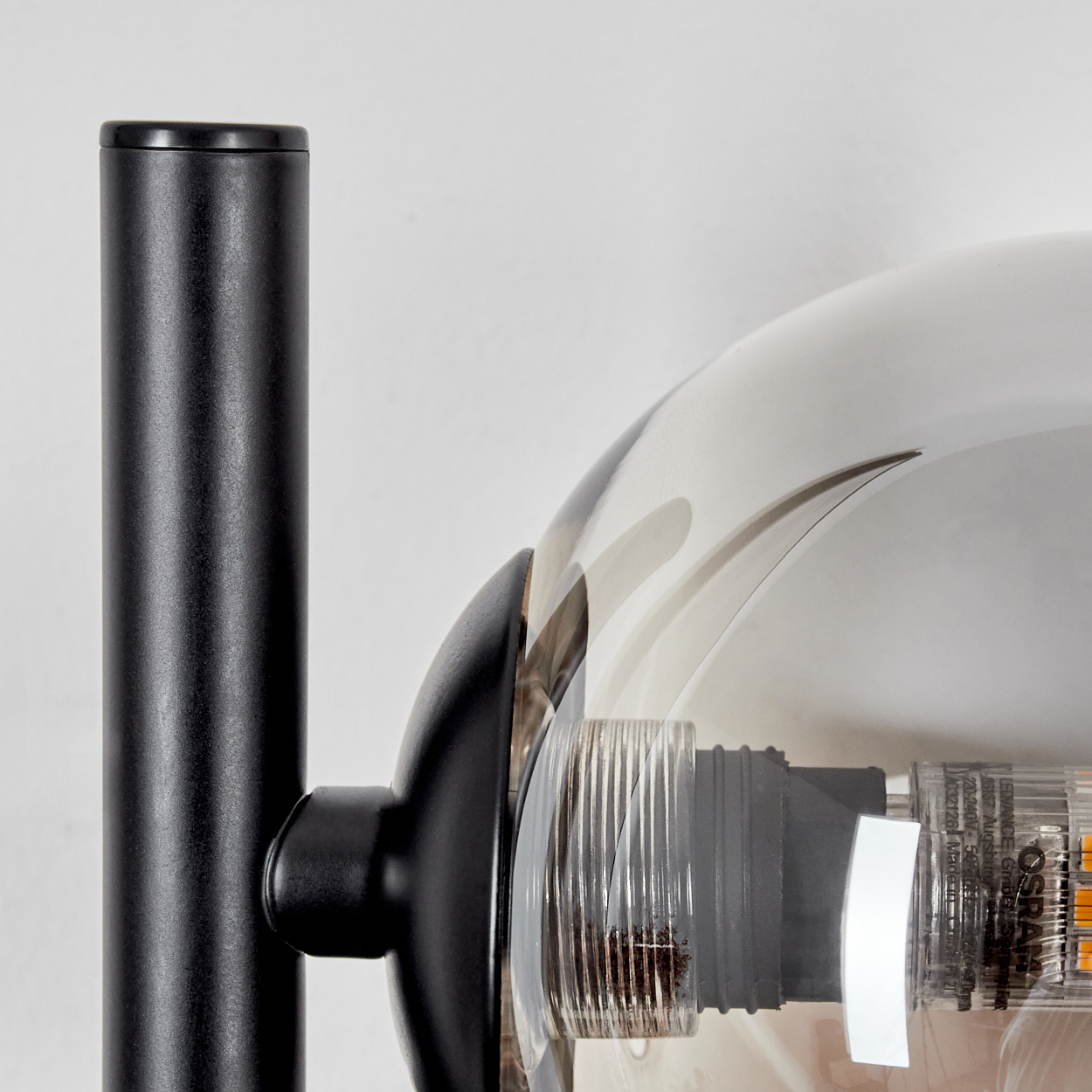 Nahaufnahme einer schwarzen Lampenstange mit einer kugelförmigen, transparenten Lampe. Die Lampe zeigt die Glühbirne.