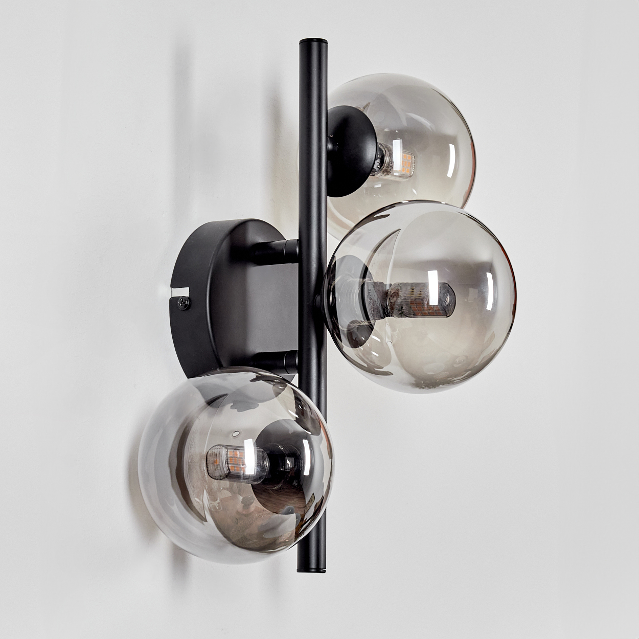 Wandlampe mit drei kugelförmigen Glasschirmen, schwarze Halterung. Von der Seite betrachtet.