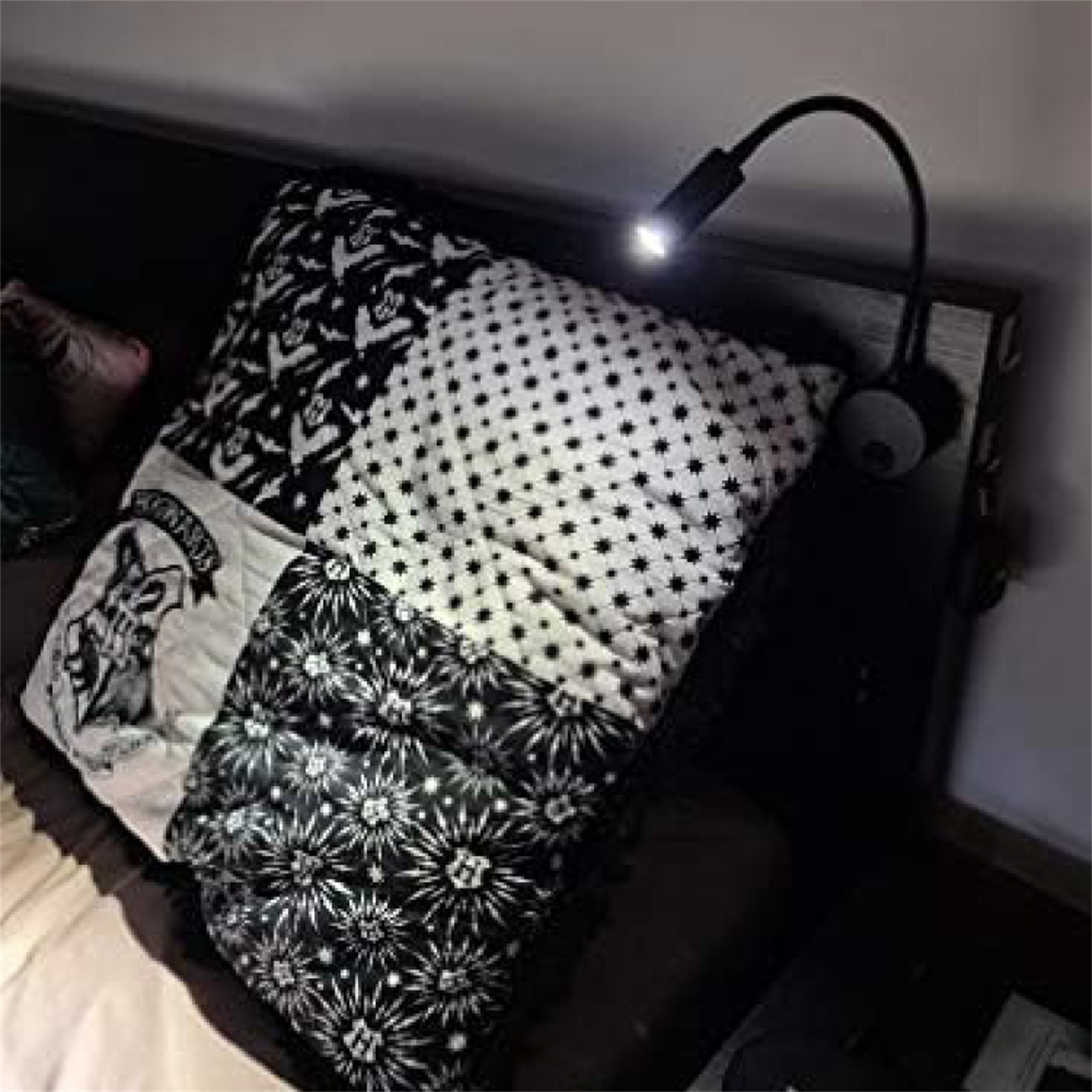 Bett mit gemustertem Kissen und Leselampe. Das Kissen hat Fledermäuse und Sterne. Die Lampe ist schwarz.