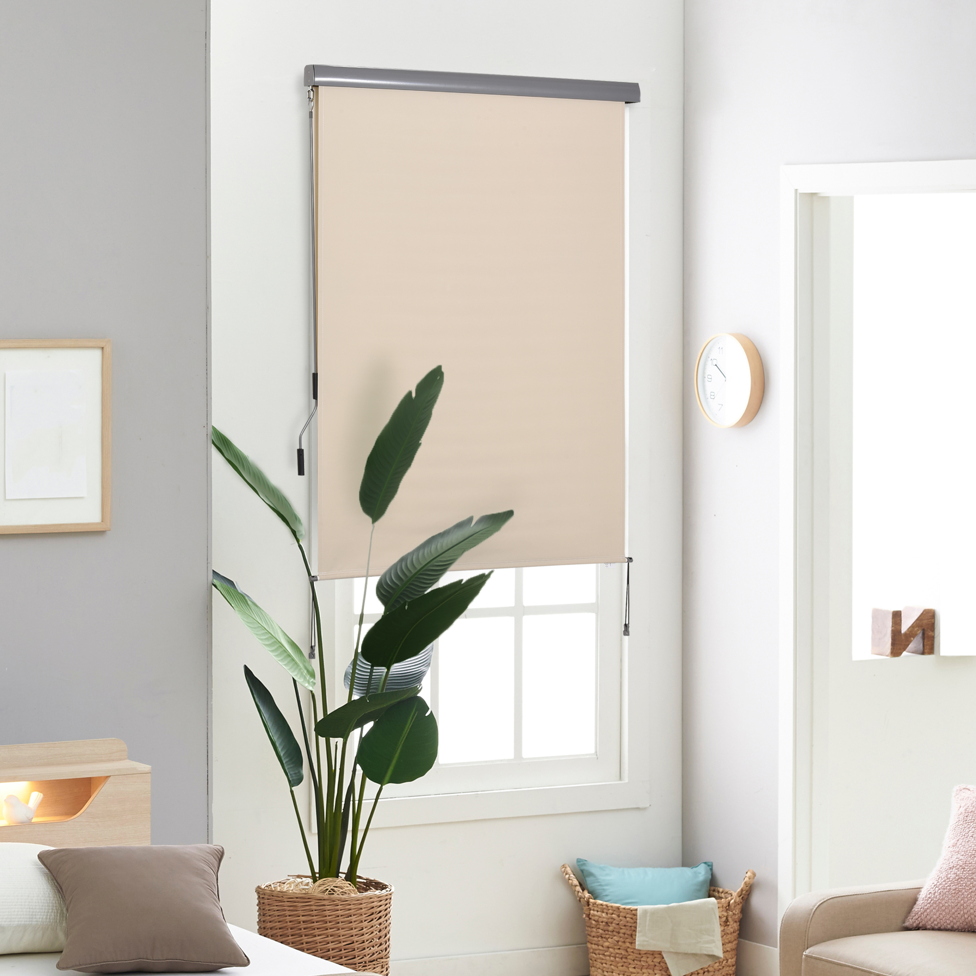 Ein beiges Rollo in einem Raum. Dahinter ein Fenster, eine Pflanze im Korb und ein Sofa.