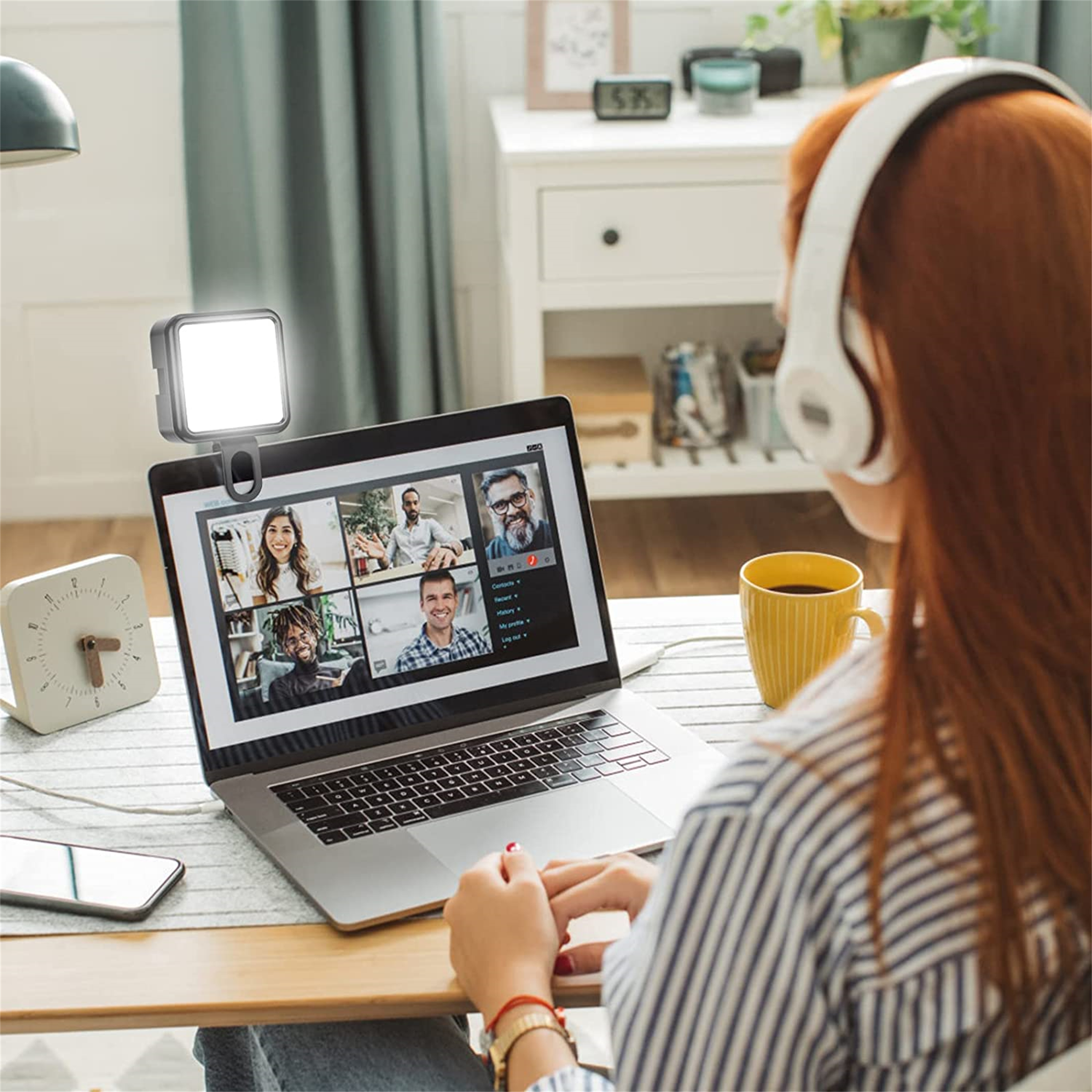 Frau bei einem Videoanruf, mit Laptop, Licht und Kopfhörern. Eine gelbe Tasse steht auf einem Schreibtisch.
