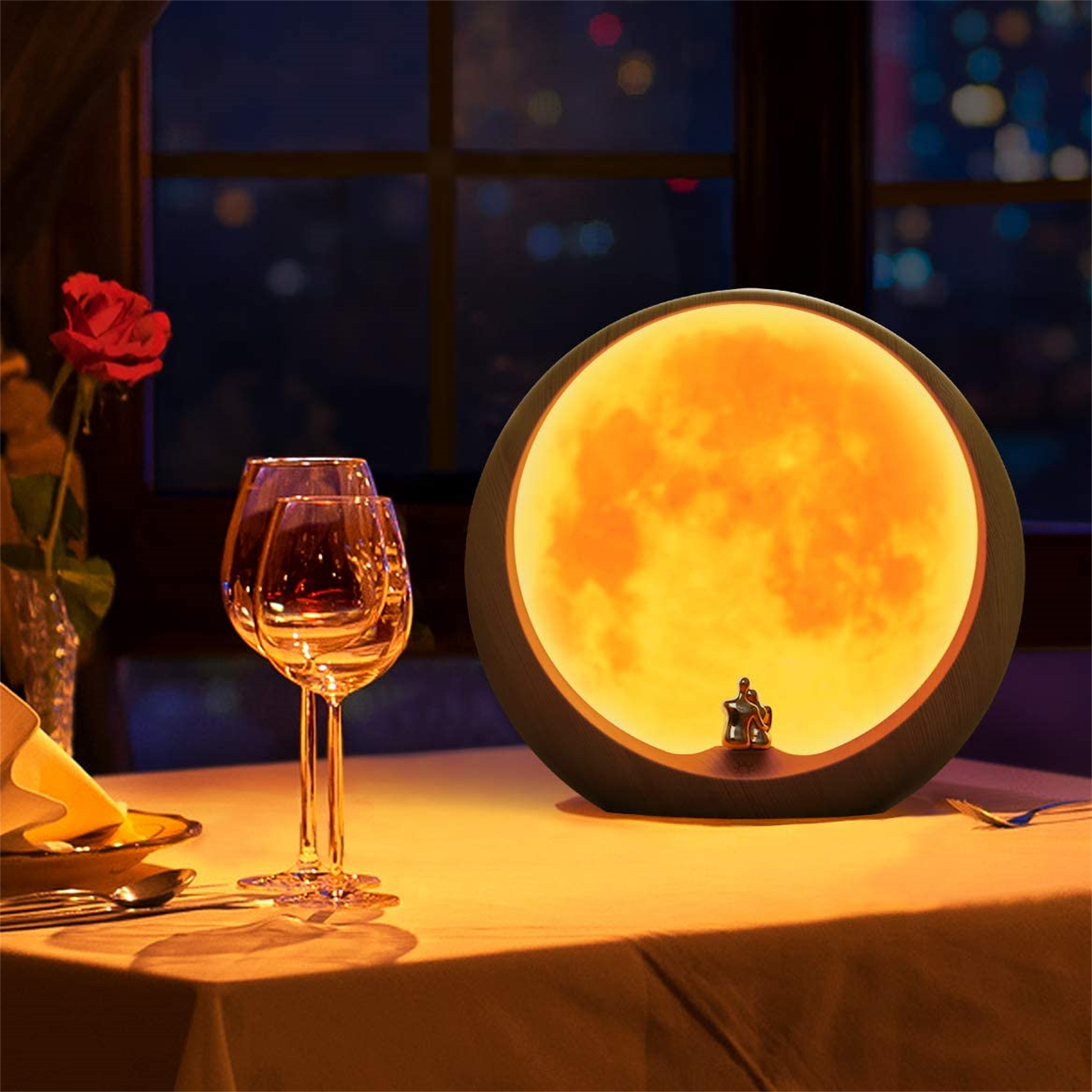 Ein gedeckter Tisch in einem Restaurant mit einer mondförmigen Lampe. Weingläser und eine Rose im Bild.