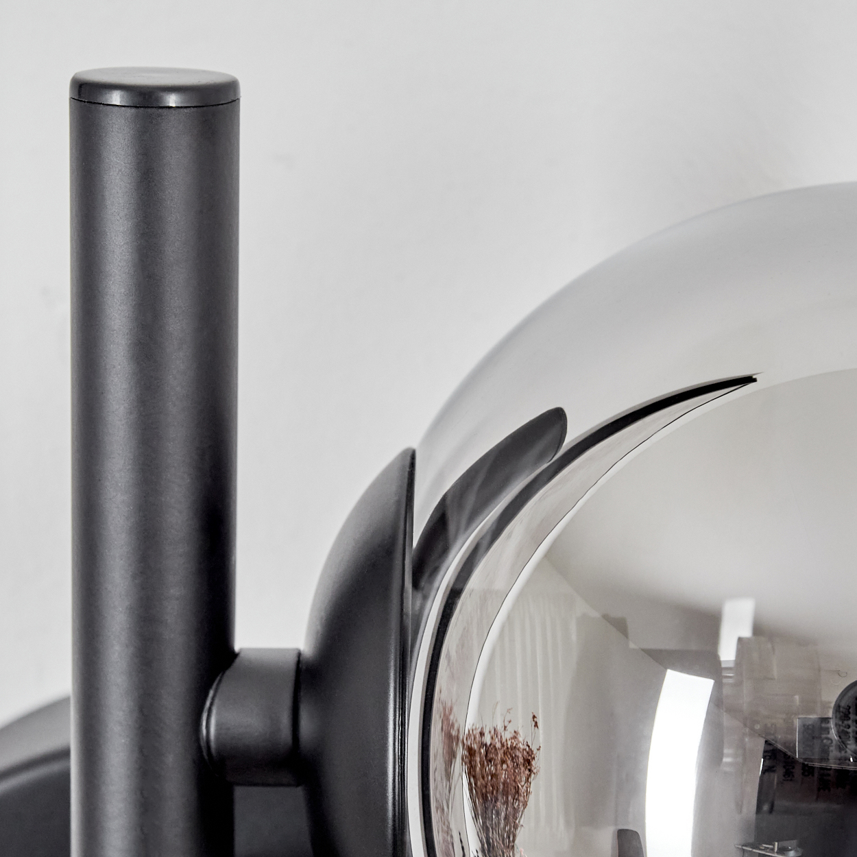 Nahaufnahme des Arms einer schwarzen Lampe und einer reflektierenden Glaskugel. Die Kugel reflektiert einen Raum.