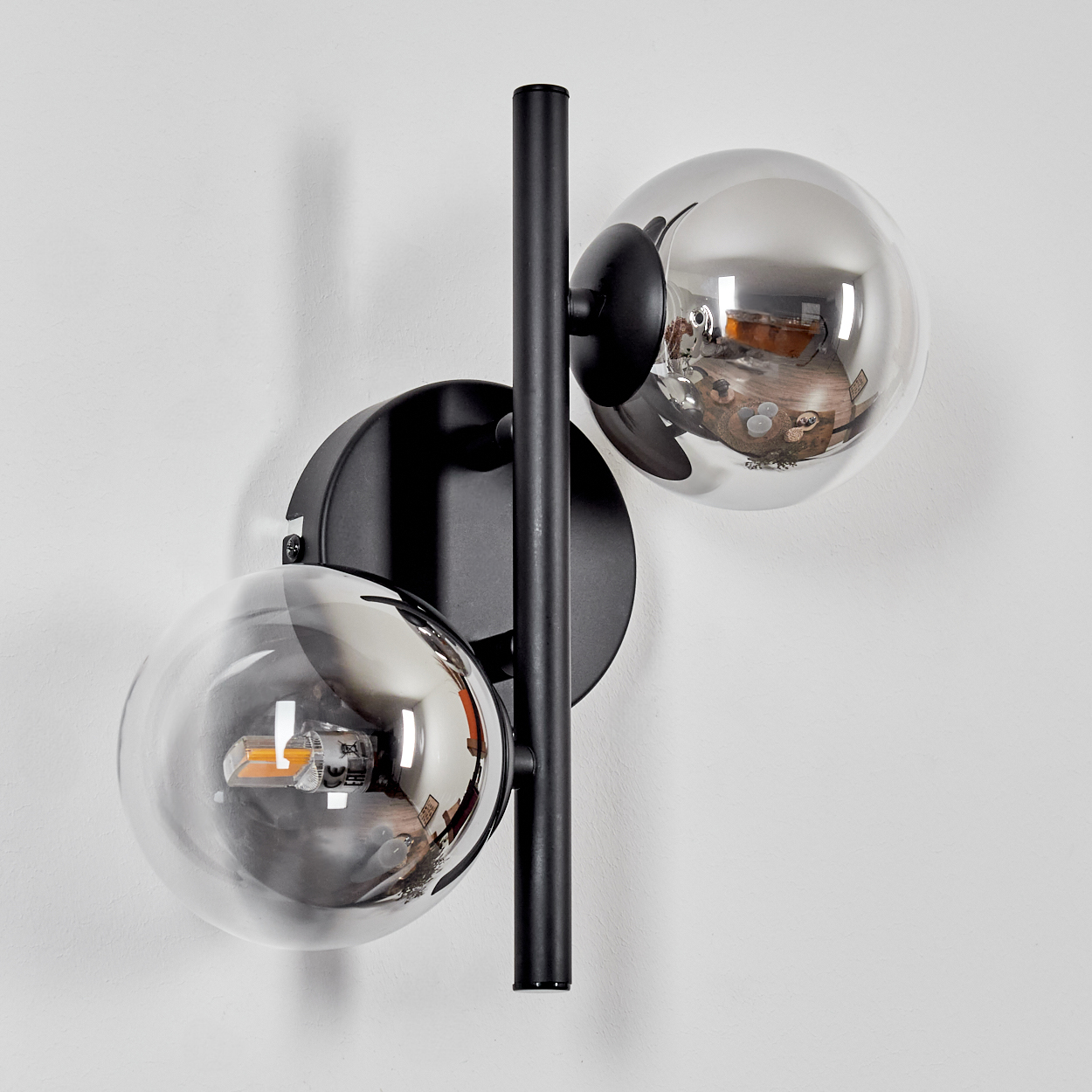 Eine Wandlampe mit zwei reflektierenden Glaskugeln. Ein schwarzer Träger befindet sich in der Mitte und die Wand ist weiß.