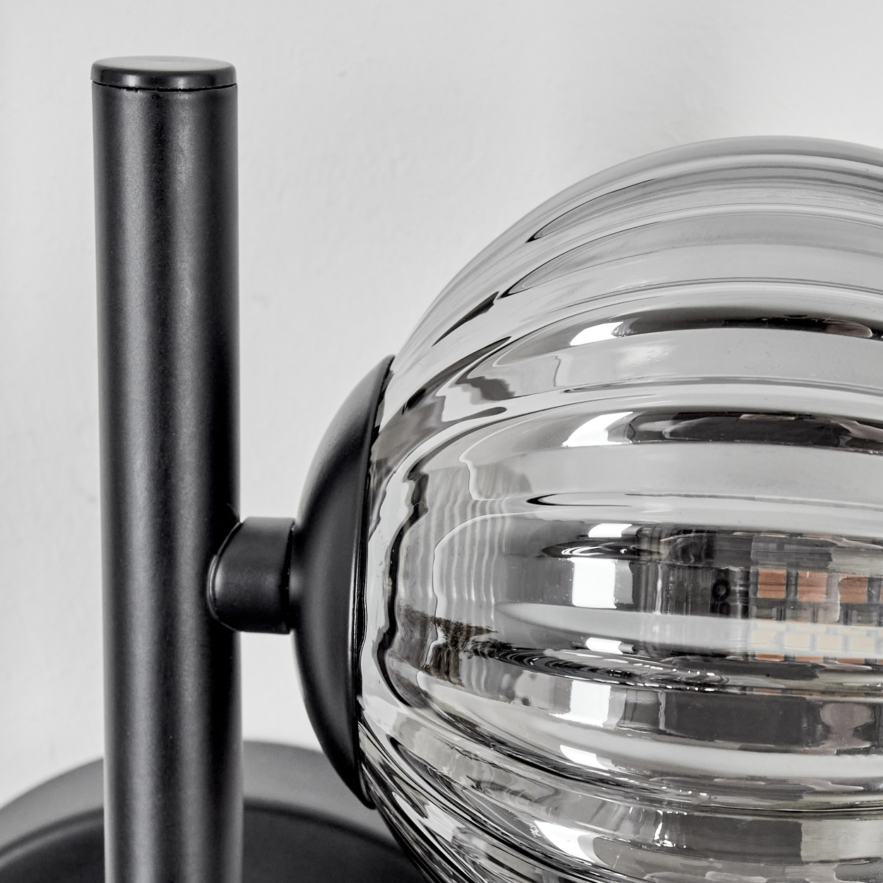 Nahaufnahme einer Wandlampe mit schwarzem Rahmen und einer geriffelten Glaskugel.