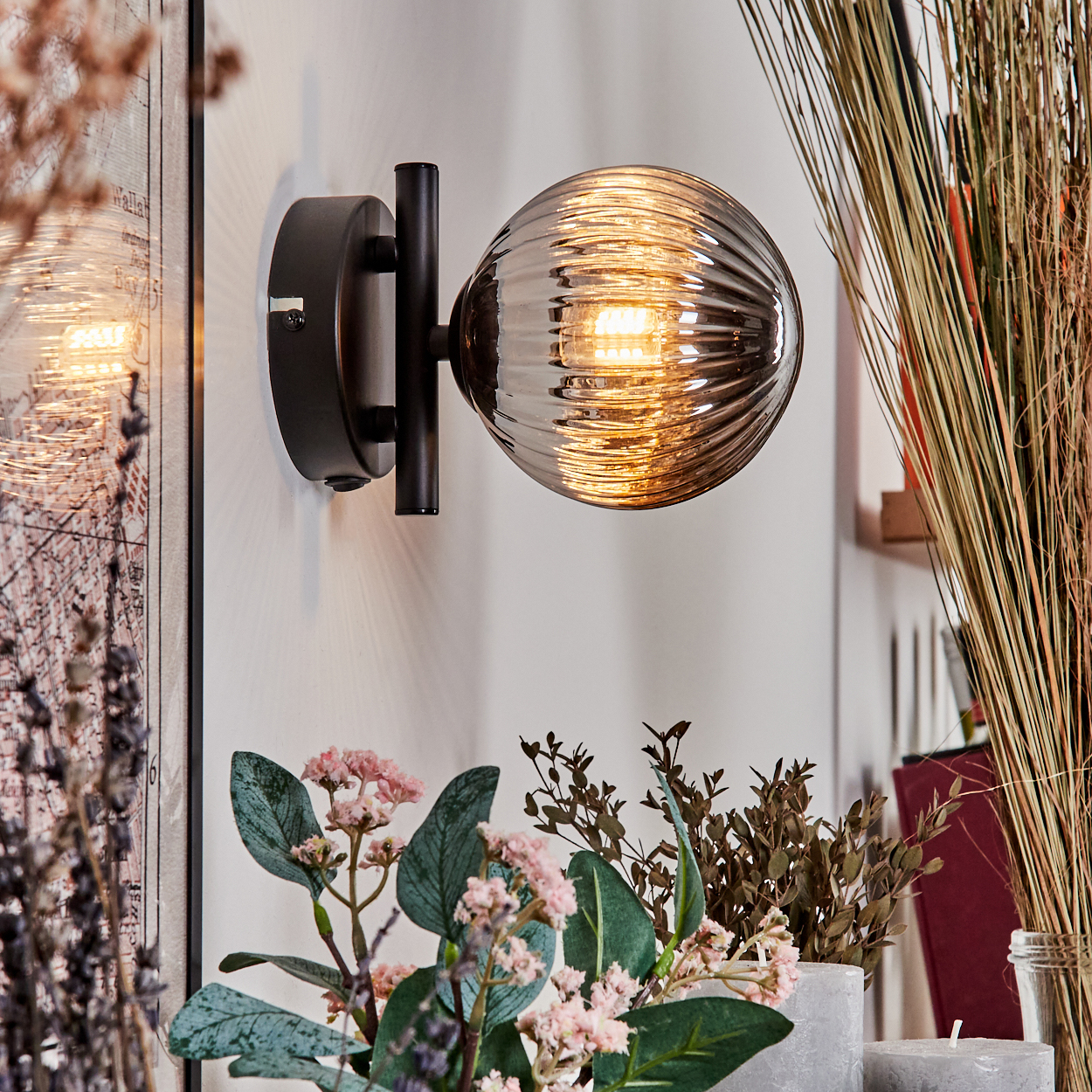 Eine Wandlampe mit einer gerippten Glaskugel, die Licht aussendet, vor einer weißen Wand mit Dekor.