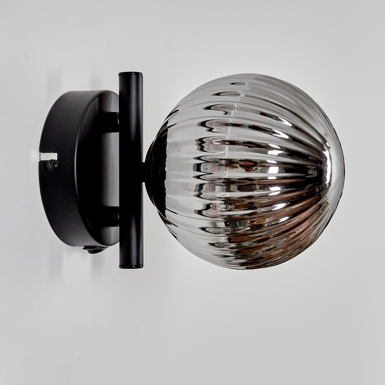 Nahaufnahme einer schwarzen Wandlampe mit einer gerippten, silberfarbenen Glaskugel an einer weißen Wand.